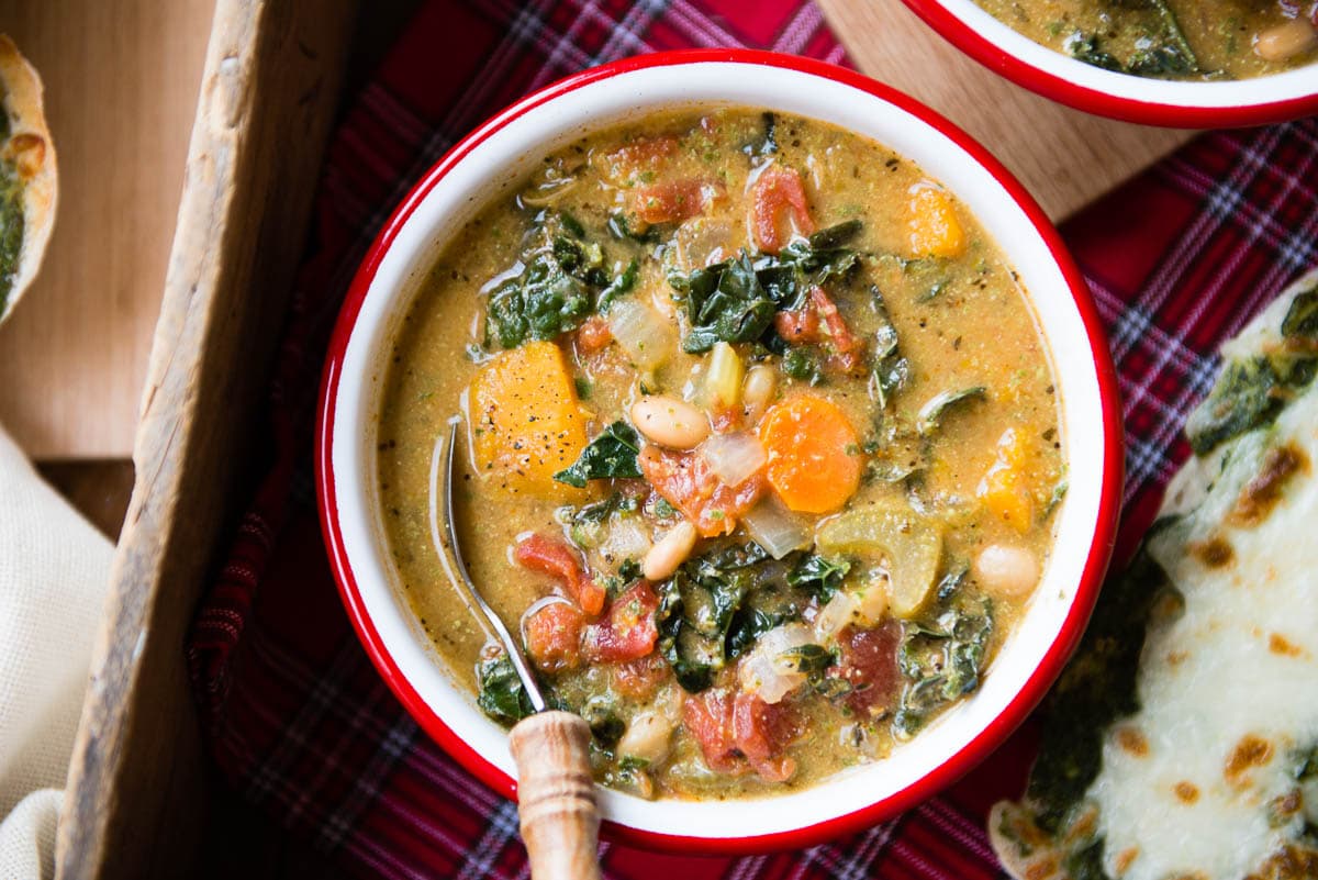 loaded vegan minestrone soup in a red and white bowl with a spoon.