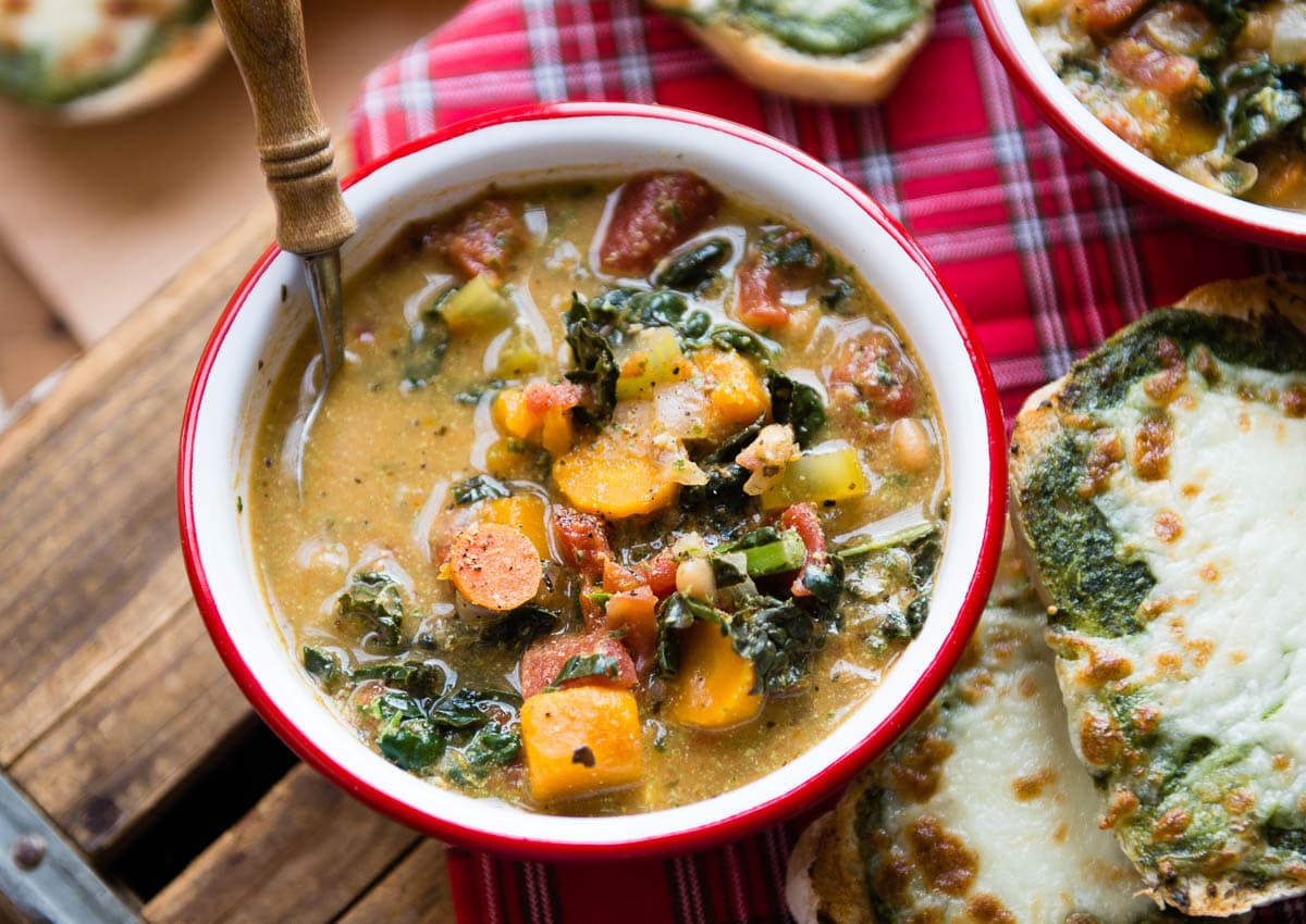 Hearty vegan minestrone soup alongside thick cheesy bread.