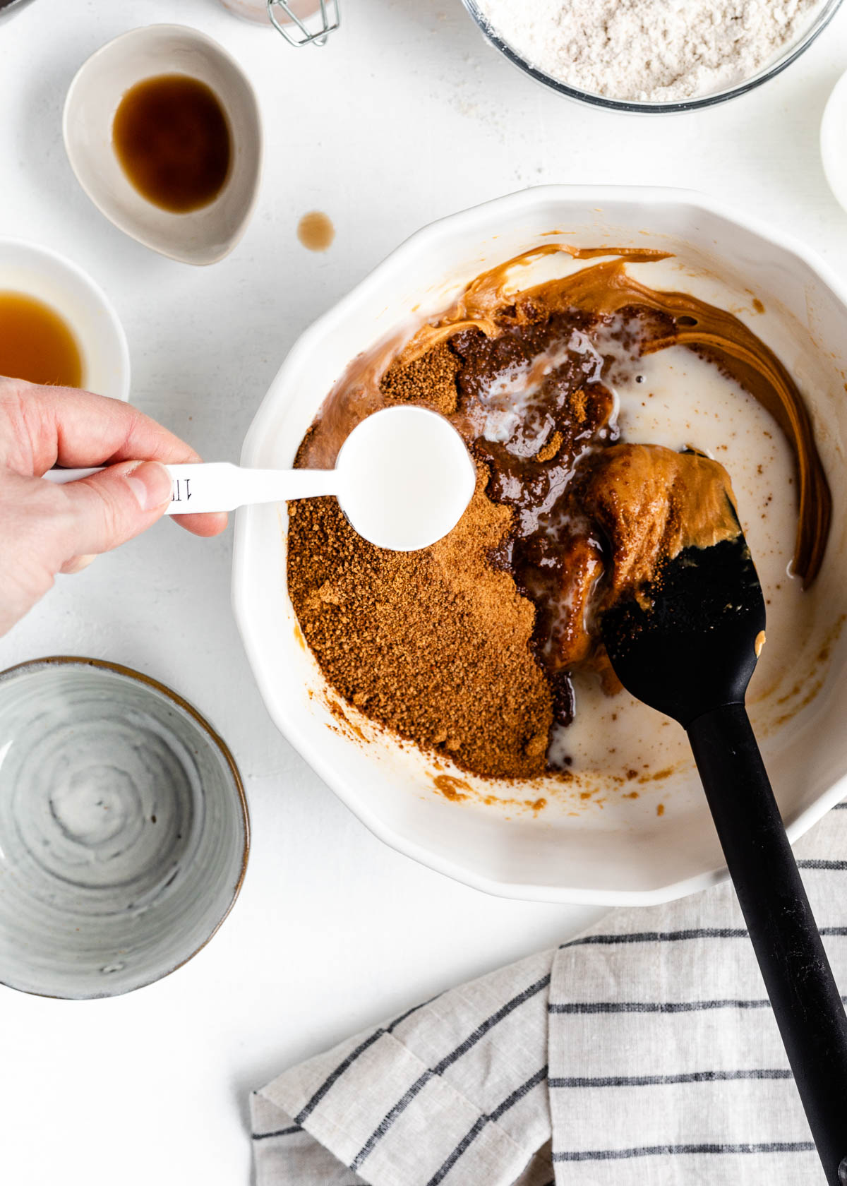 white measuring spoon adding salt and baking soda to bowl of ingredients, ready to be combined with a black spatula.