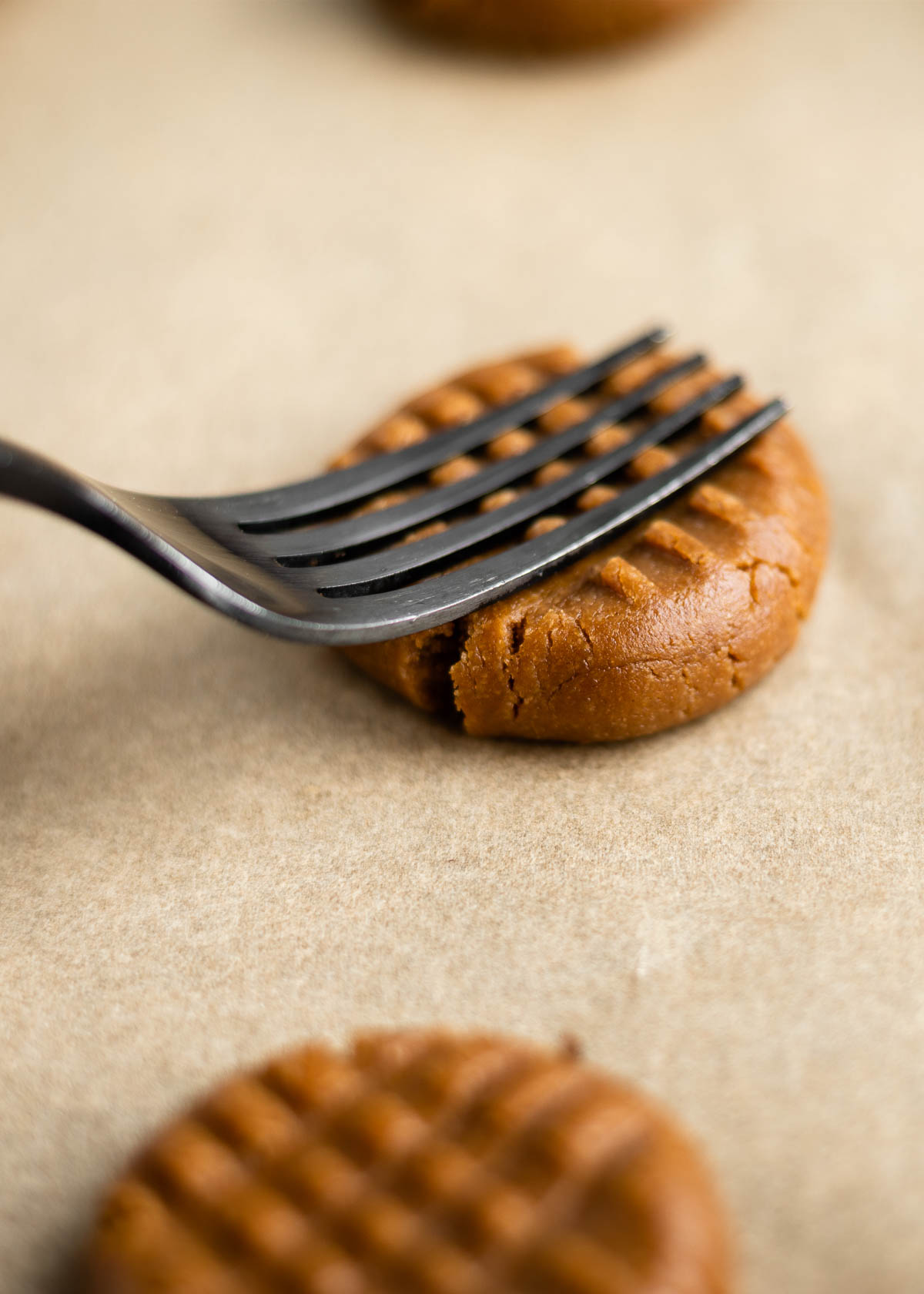 a fork pressing down on cookie dough to form the criss cross pattern of traditional peanut butter cookies.