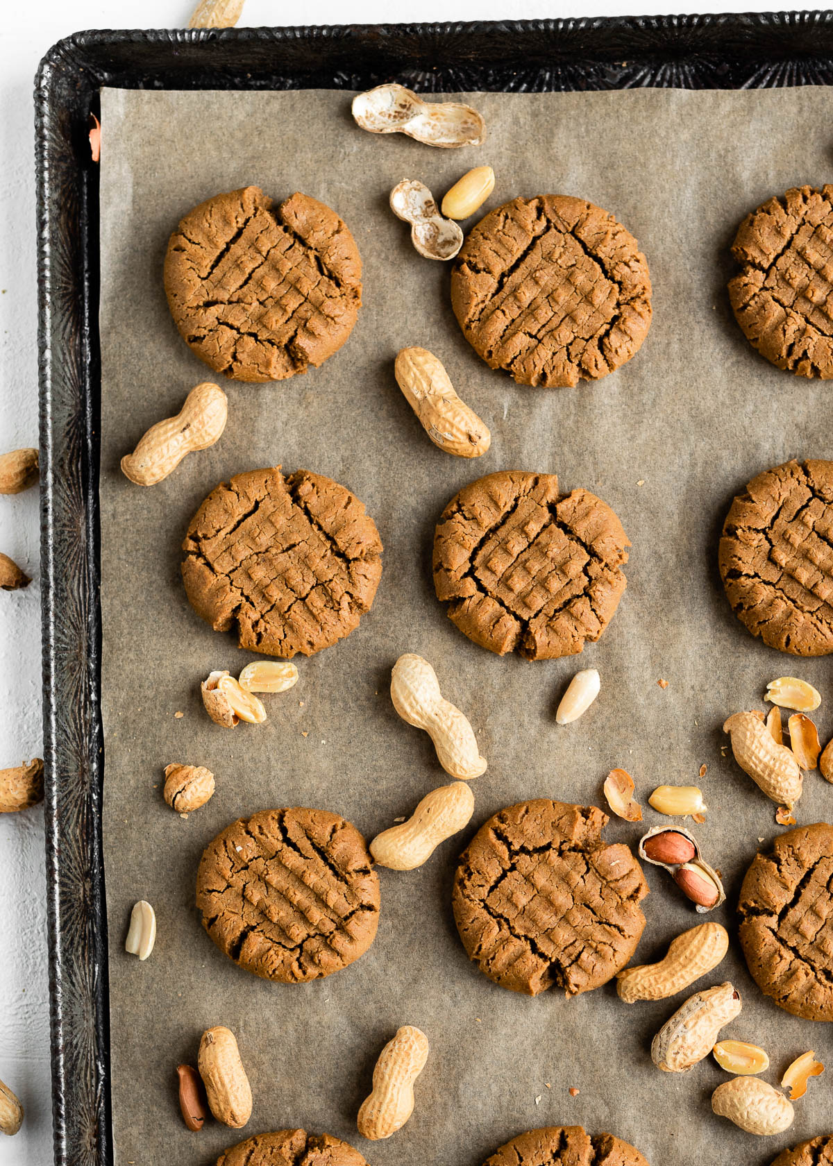finished vegan peanut butter cookies on a baking sheet, surrounded by shelled peanuts.