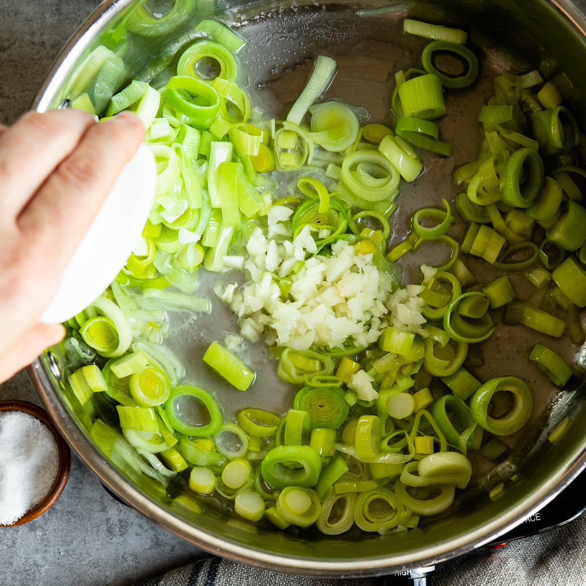 garlic being added to a pot with chopped leek