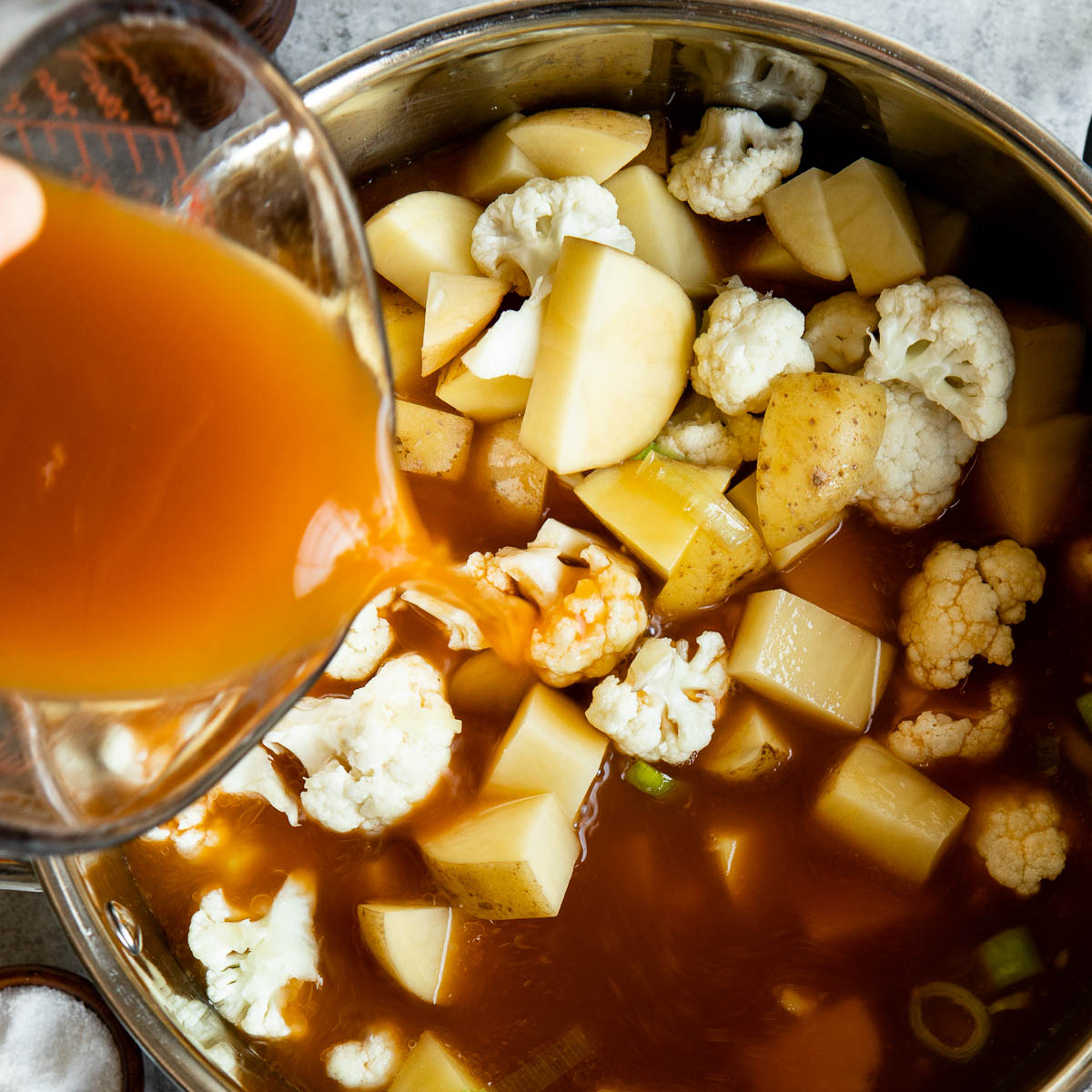 Adding broth to pot with potatos and cauliflower