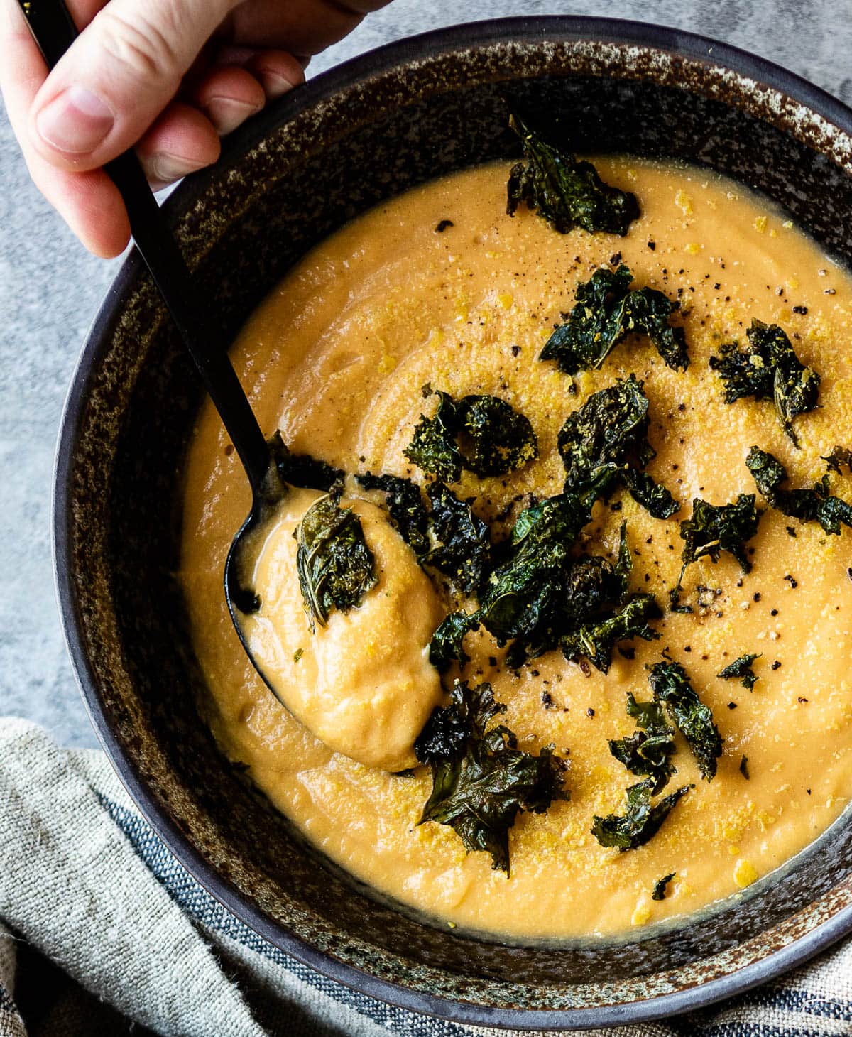 hand with spoon scooping out some delicious potato soup with kale croutons.