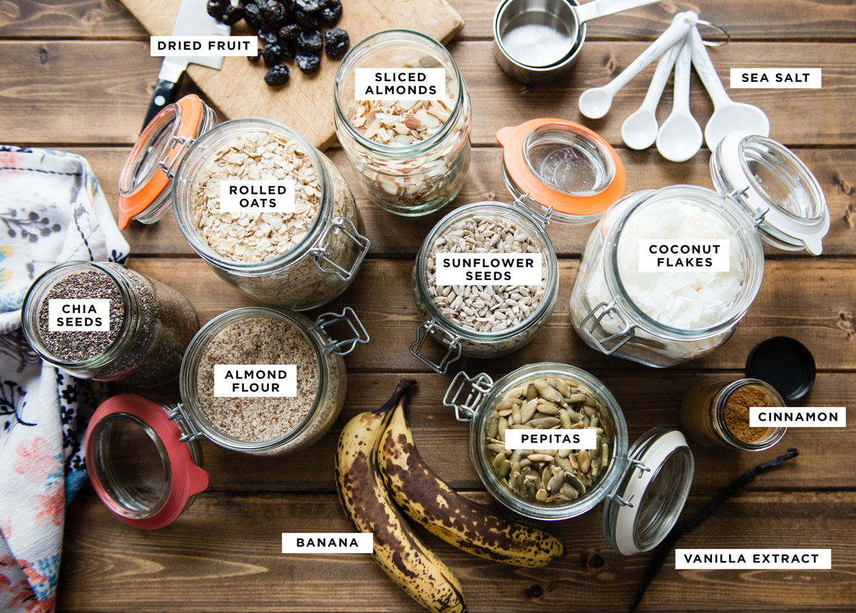labeled ingredients for a protein bar recipe including dried fruit, sliced almonds, sea salt, coconut flakes, sunflower seeds, rolled oats, chia seeds, almond flour, pepitas, cinnamon, banana and vanilla extract.