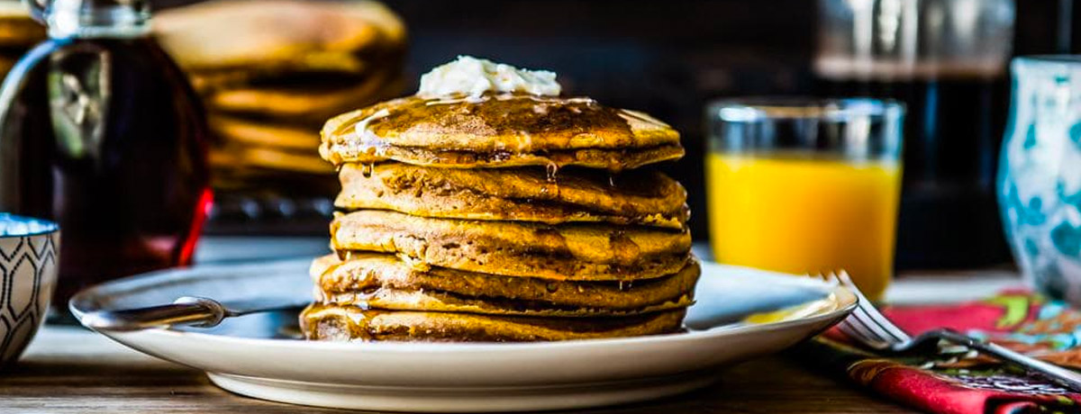 stack of pumpkin pancakes with orange juice and coffee in the background