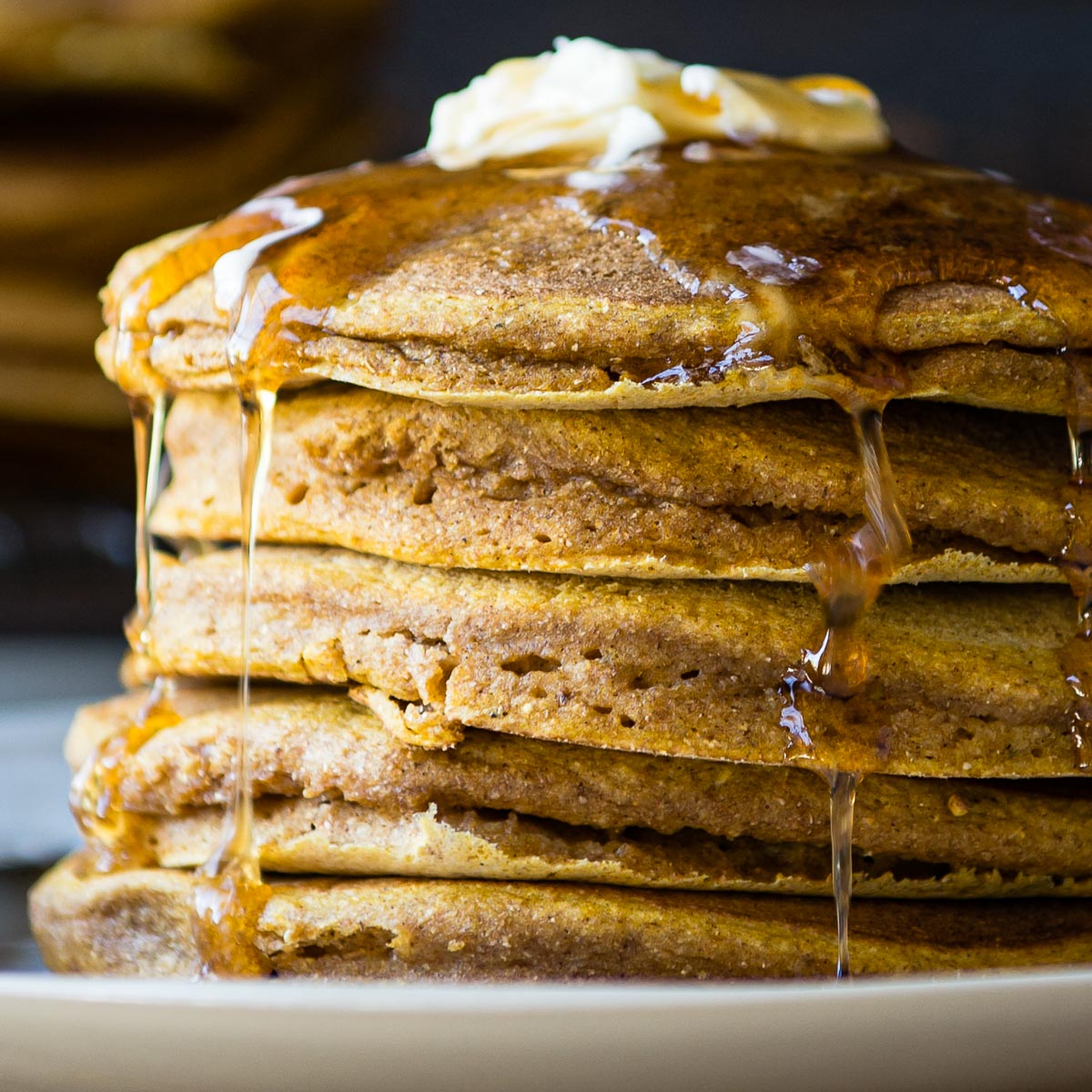 Stack of vegan pumpkin pancakes dripping with syrup.