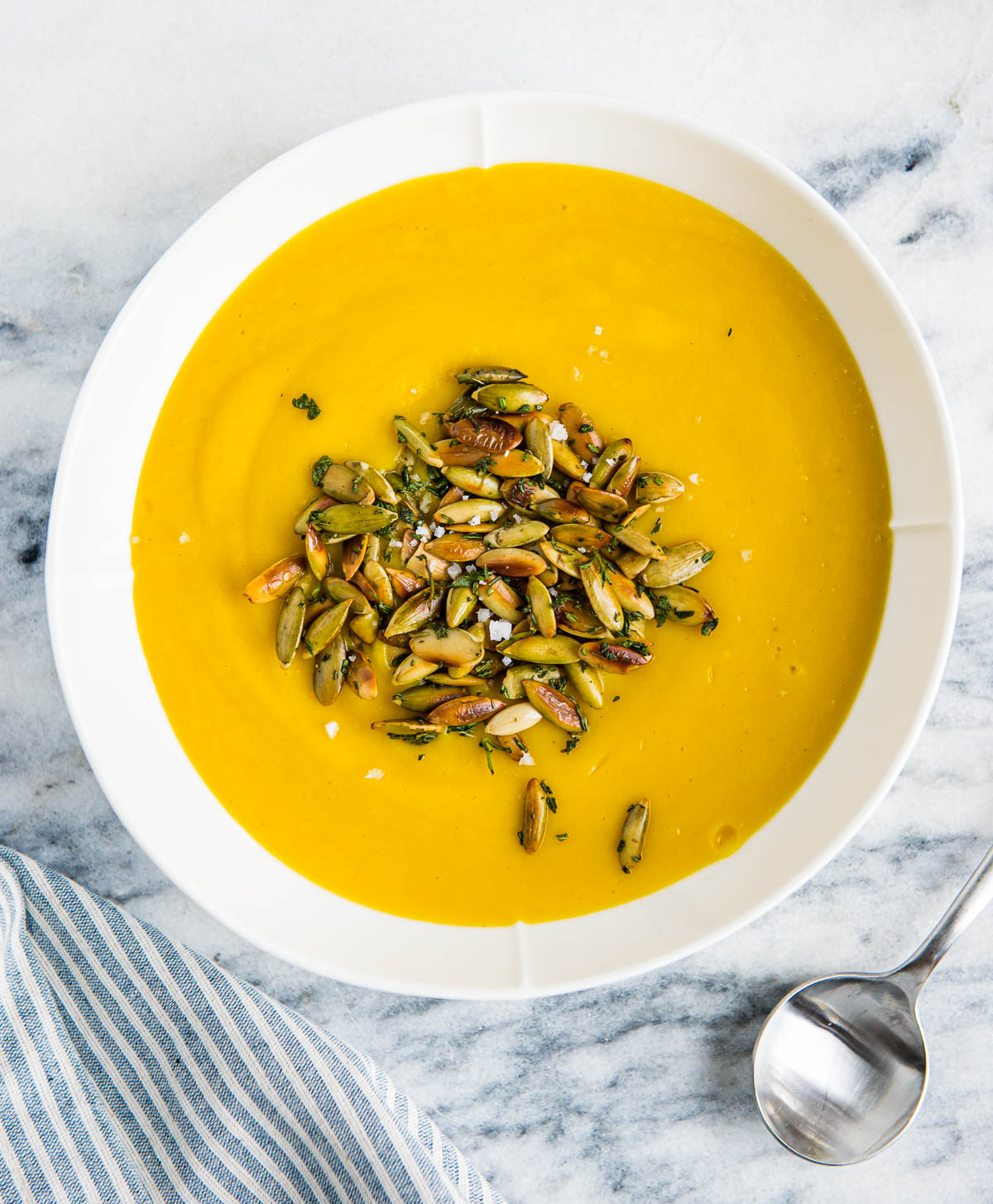 white bowl full of vegan pumpkin soup topped with roasted pumpkin seeds, on a marble counter top.