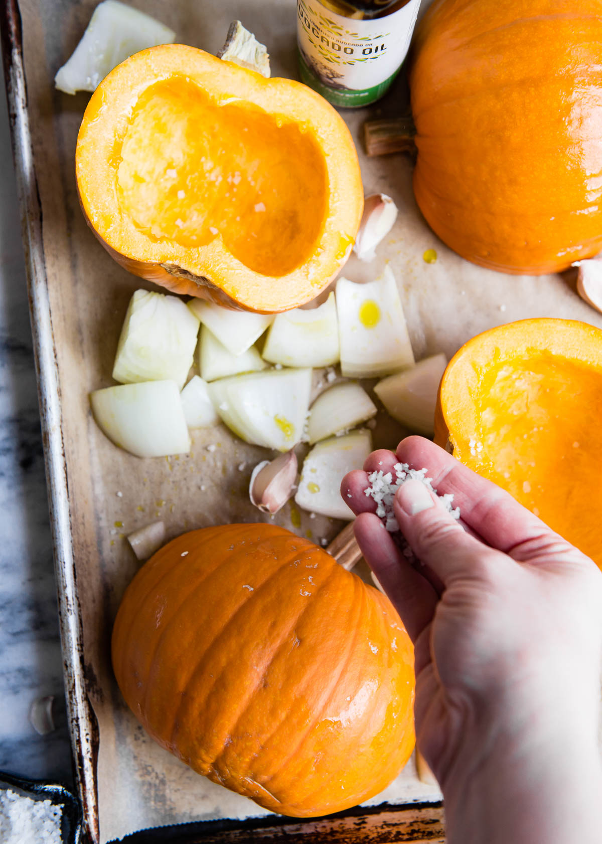 one hand sprinkling coarse sea salt over a pan of pie pumpkins and onions.