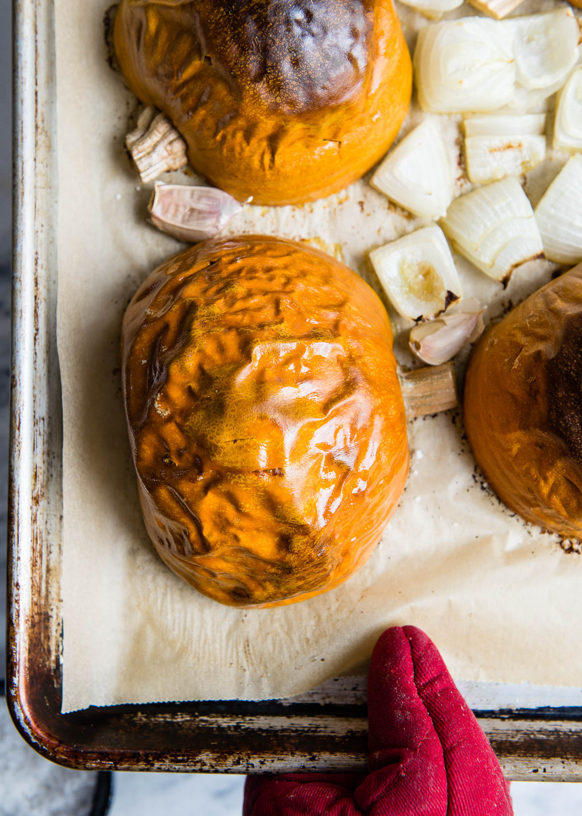 taking roasted pumpkins and onions out of the oven on a baking tray.