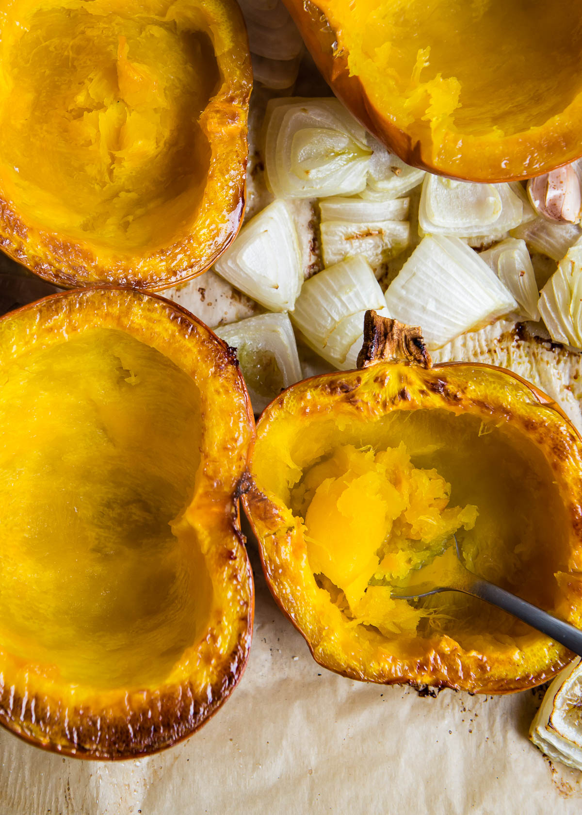 using a black spoon to scoop the flesh out of a baked pumpkin for vegan pumpkin soup.