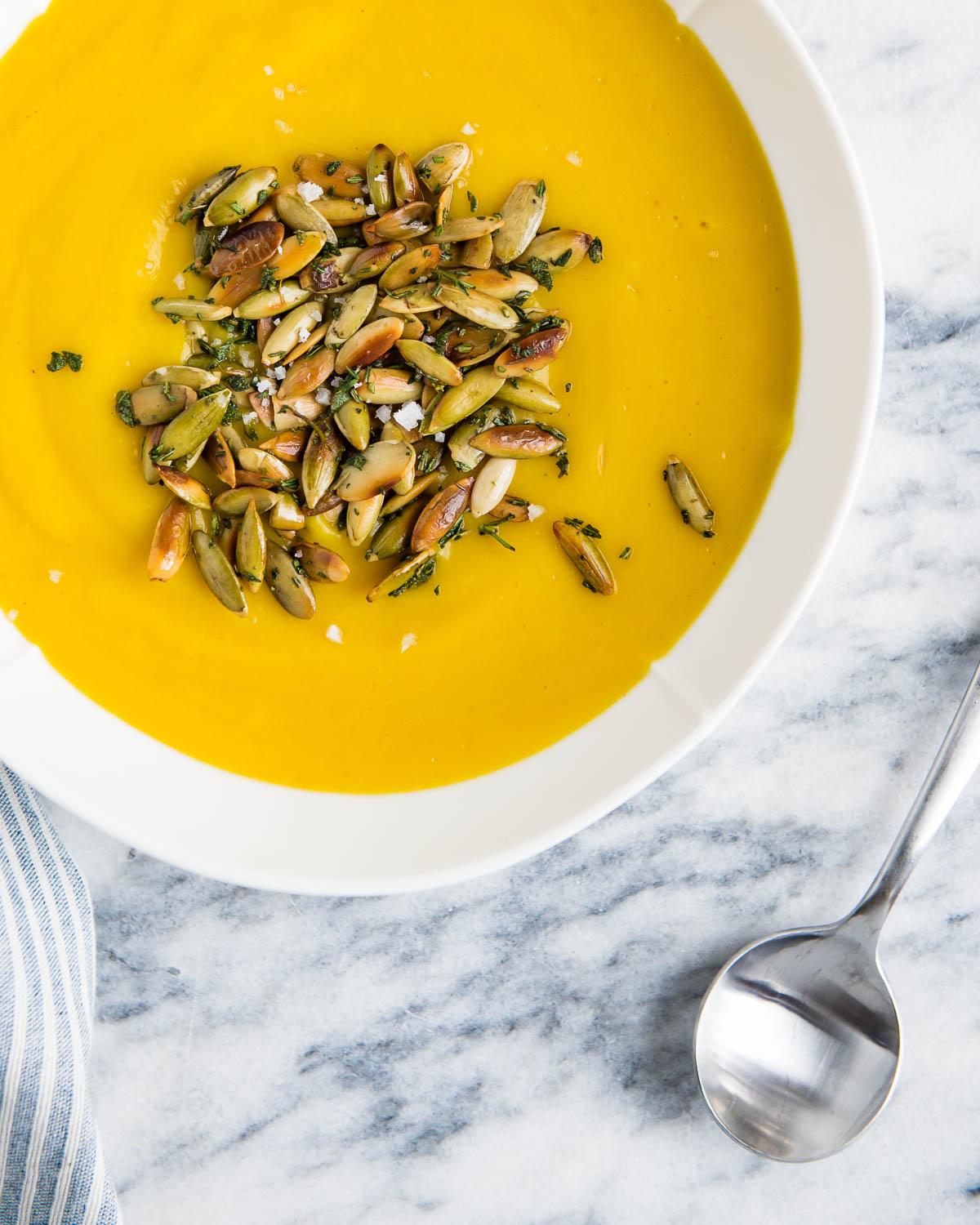 white bowl full of vegan pumpkin soup topped with roasted pumpkin seeds, on a marble counter top.