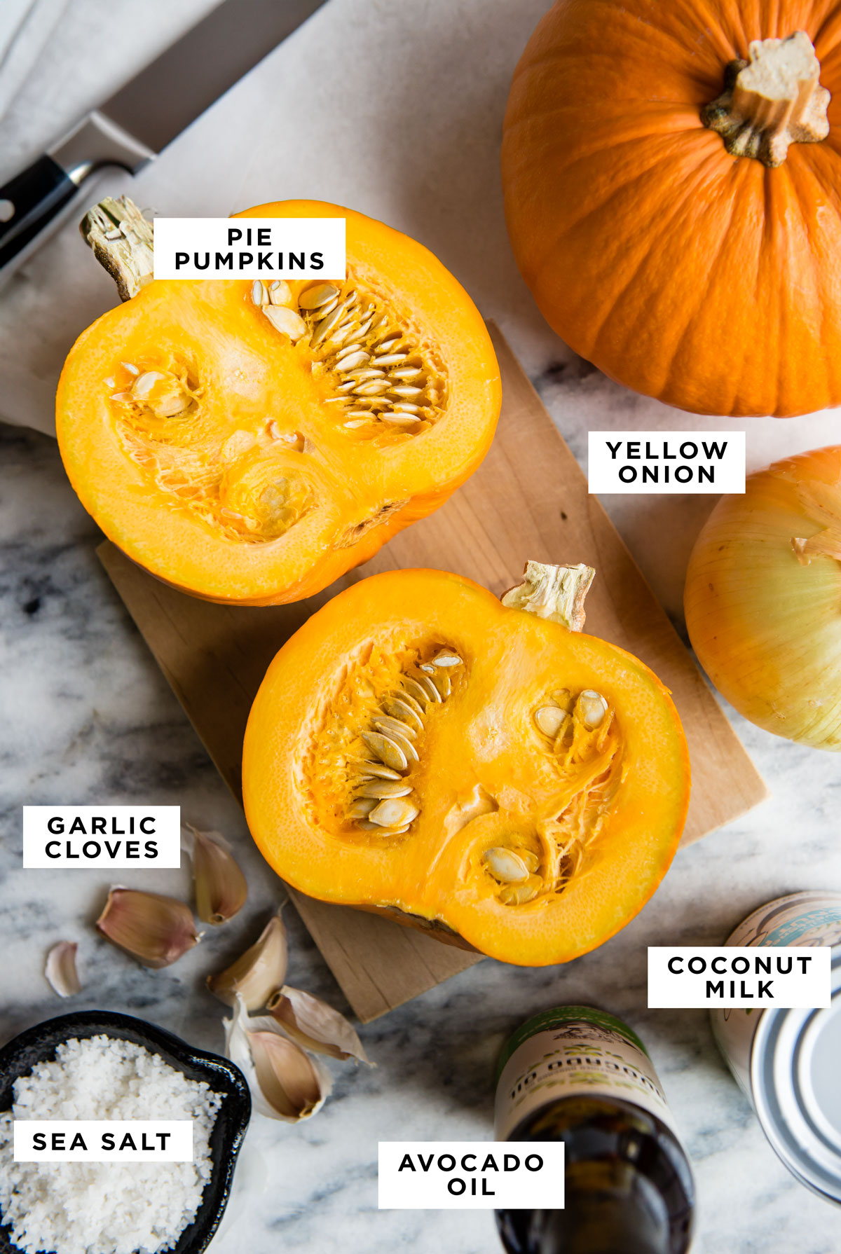 labeled ingredients for a pumpkin soup recipe including pie pumpkins, yellow onion, garlic cloves, coconut milk, sea salt and avocado oil.