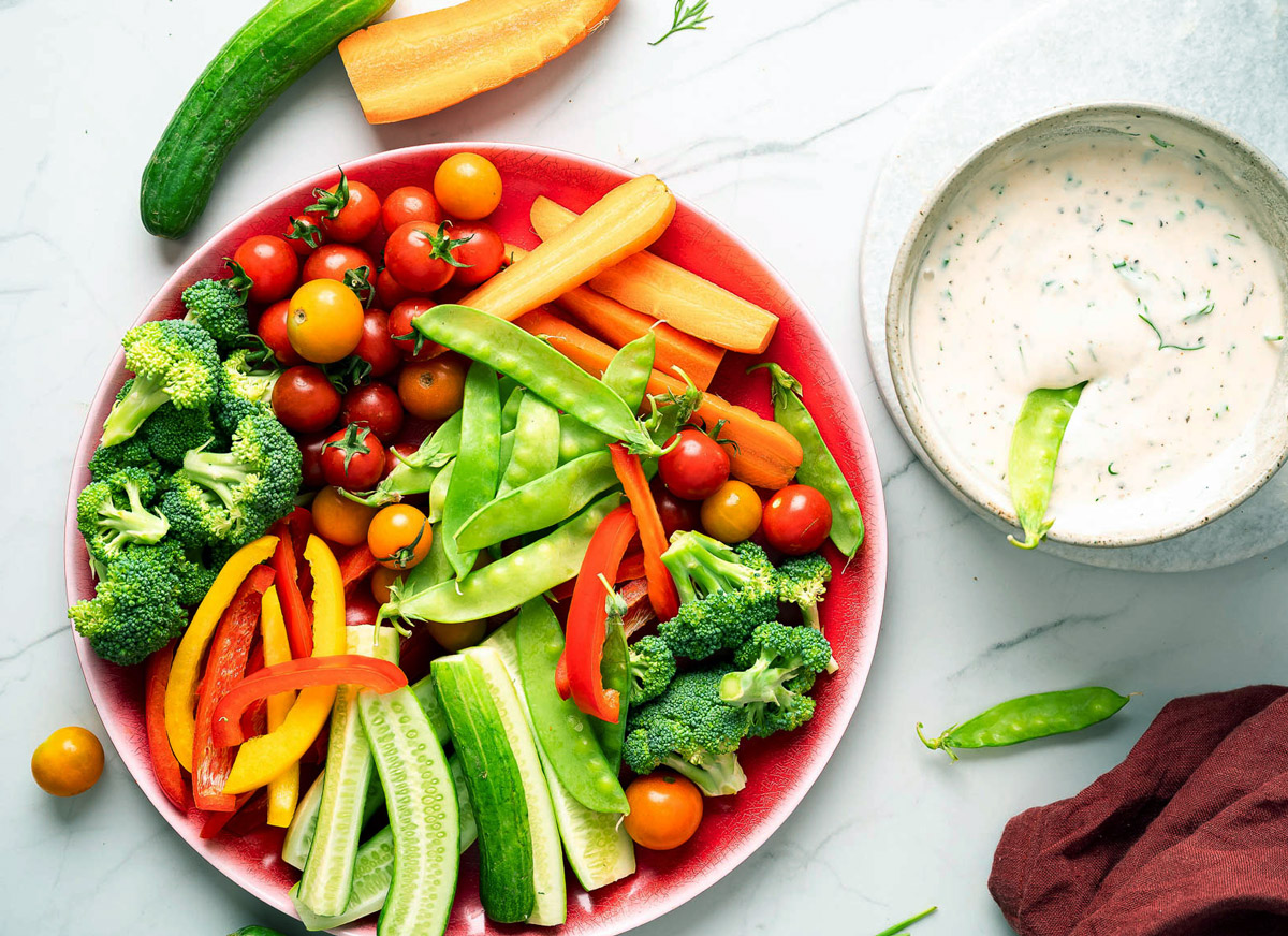 Bowl of vegan ranch dressing alongside a plate of fresh vegetables.