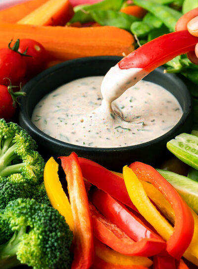 Dark bowl filled with vegan ranch dip, surrounded by colorful assortment of fresh vegetables.