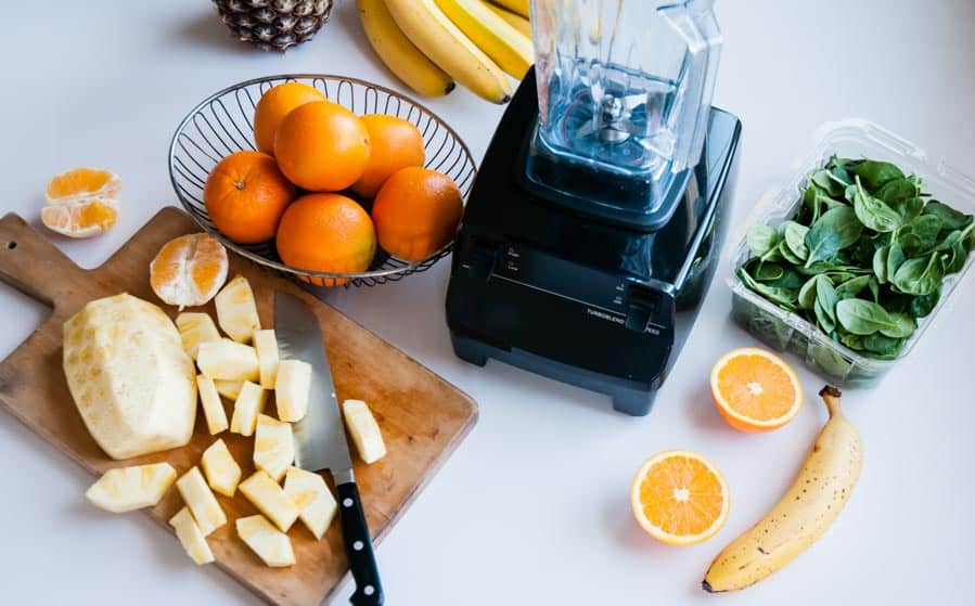 ingredients for a healthy snack including bananas, pineapple, oranges and spinach.