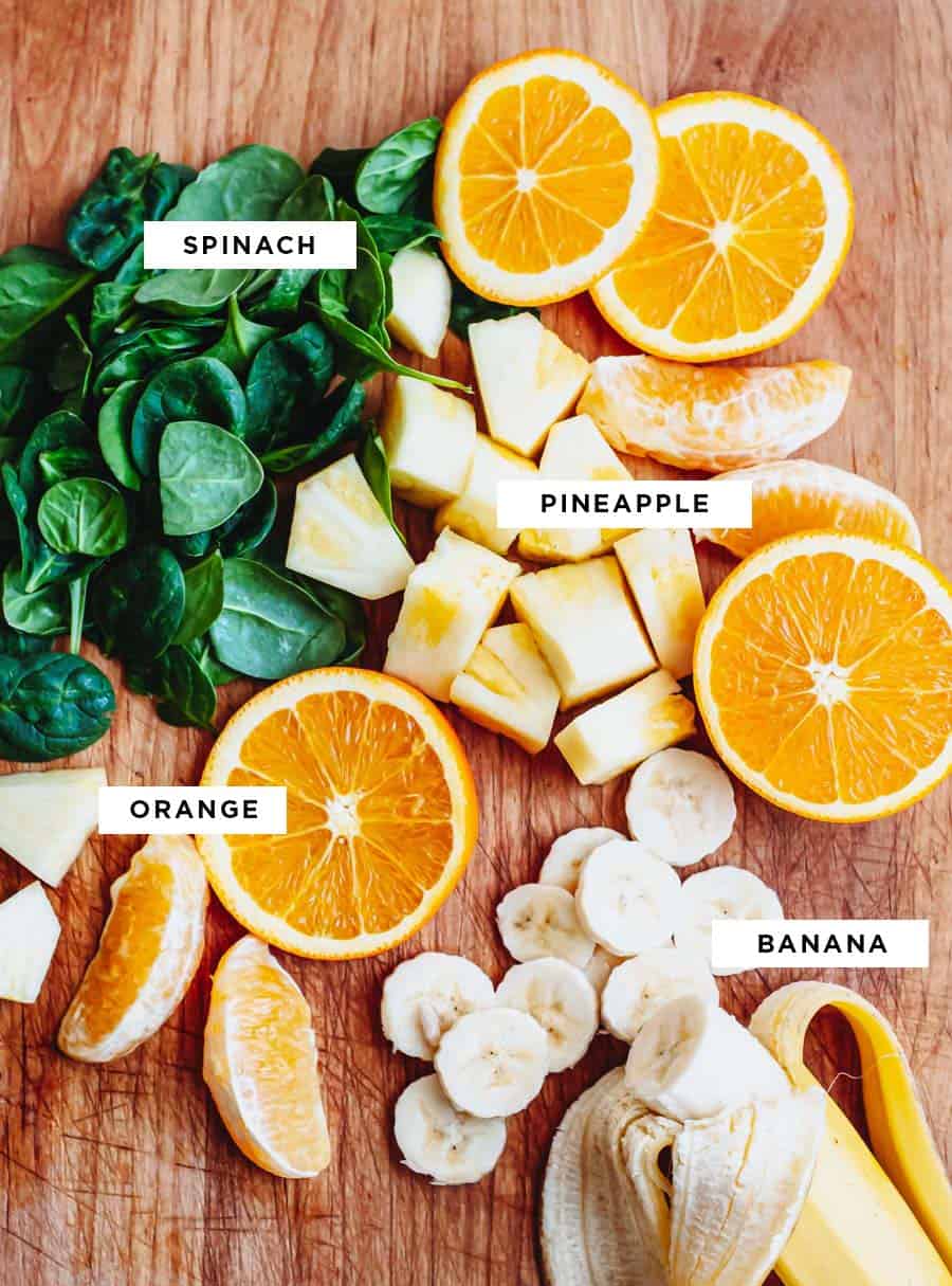 labeled ingredients for a vegan tropical smoothie including spinach, pineapple, orange and banana.