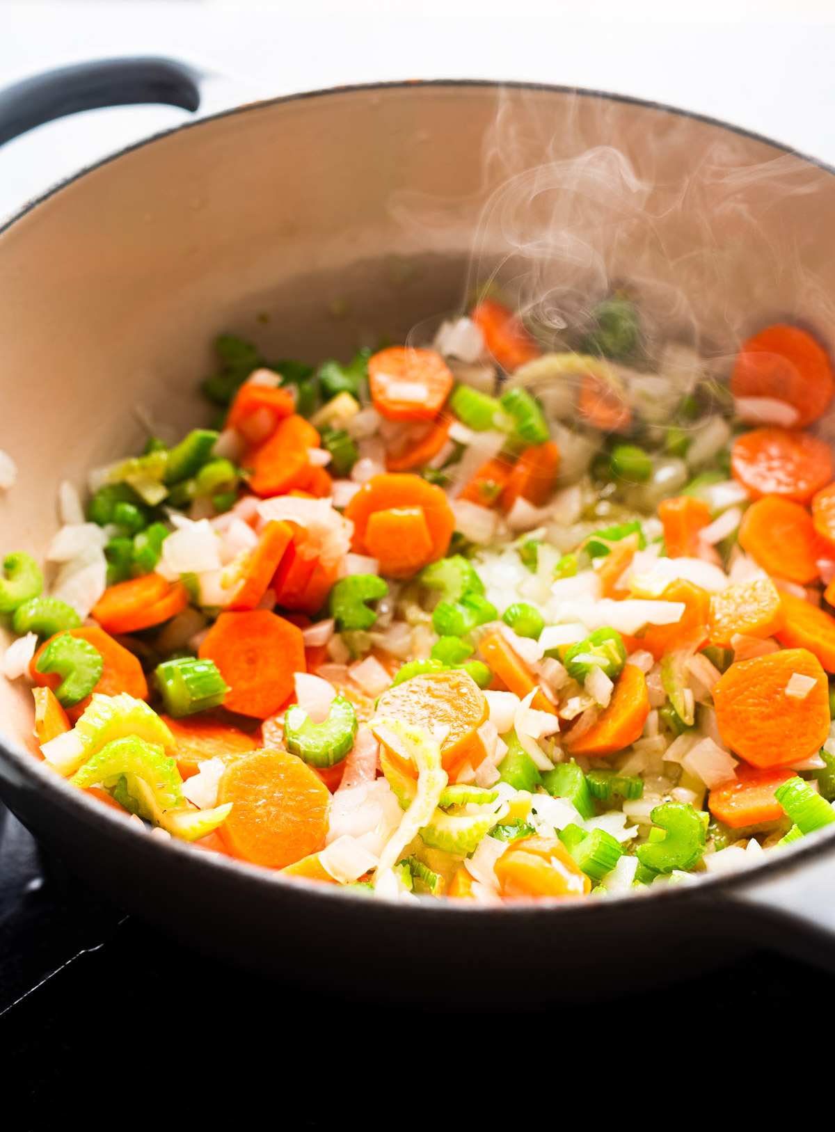 Sauteing carrots, celery and onions in a white stock pot on stove.