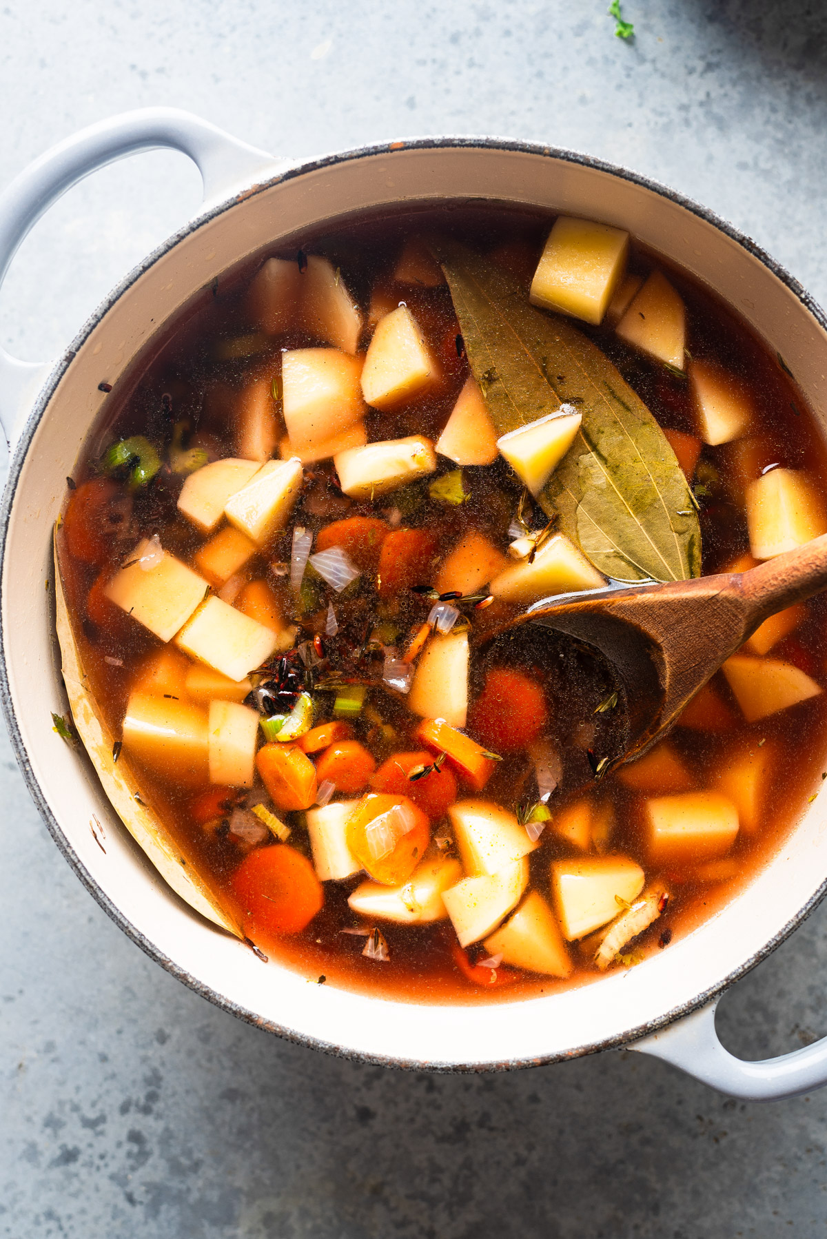 White pot full with diced potatoes, carrots and bay leaves with vegeatble stock.