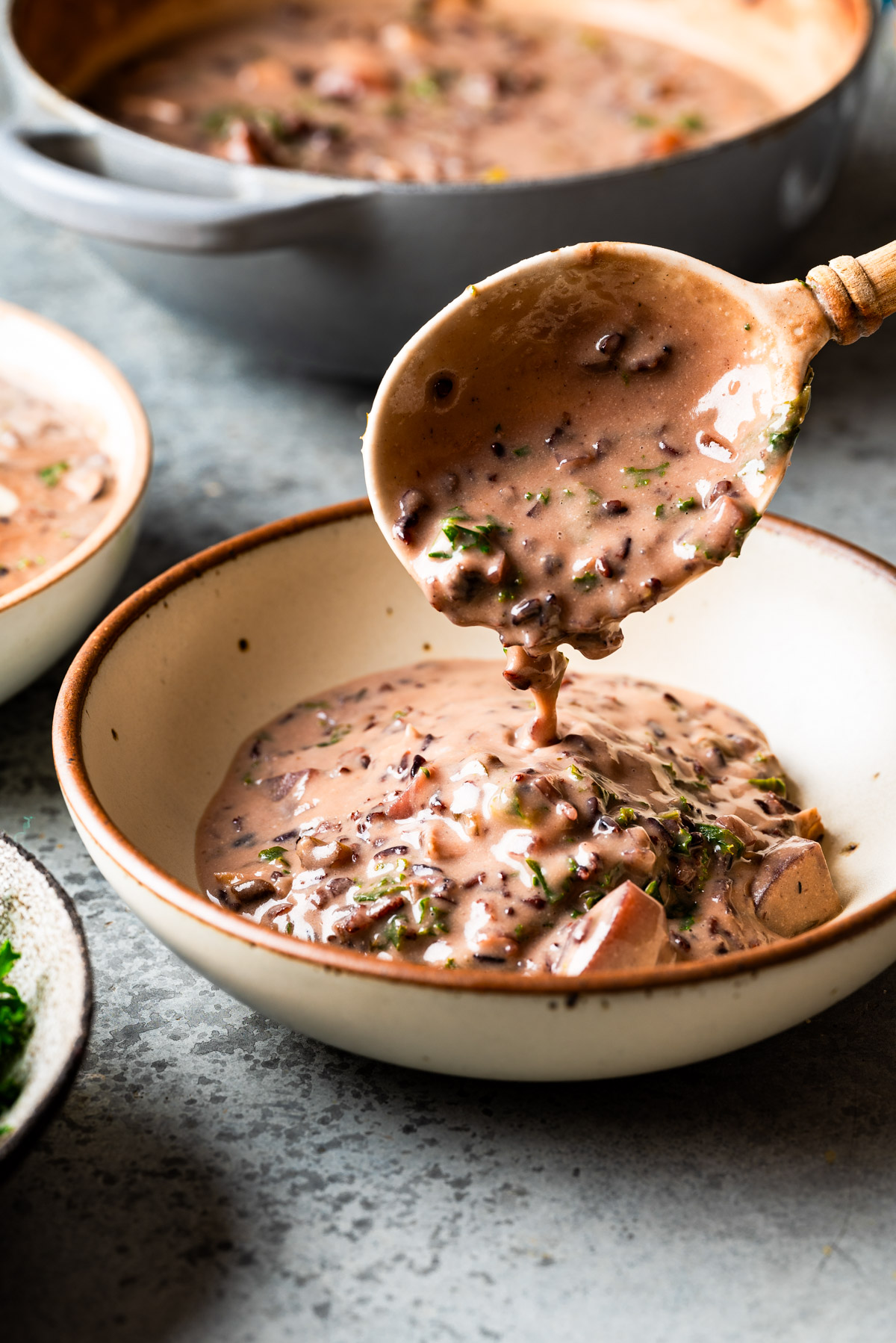 Wood spoon serving soup into a pottery bowl.