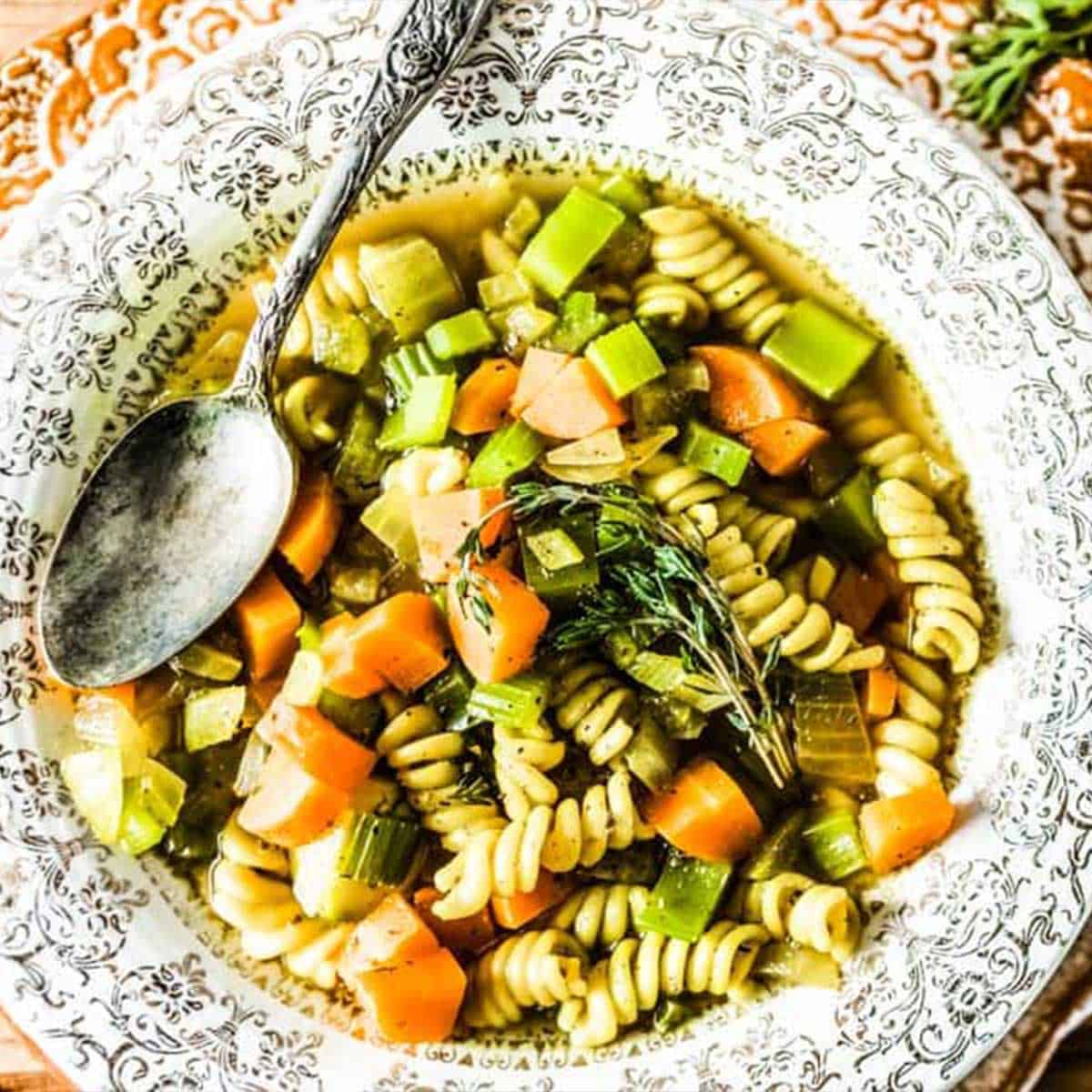 vegetable noodle soup in a festive bowl with a silver spoon.