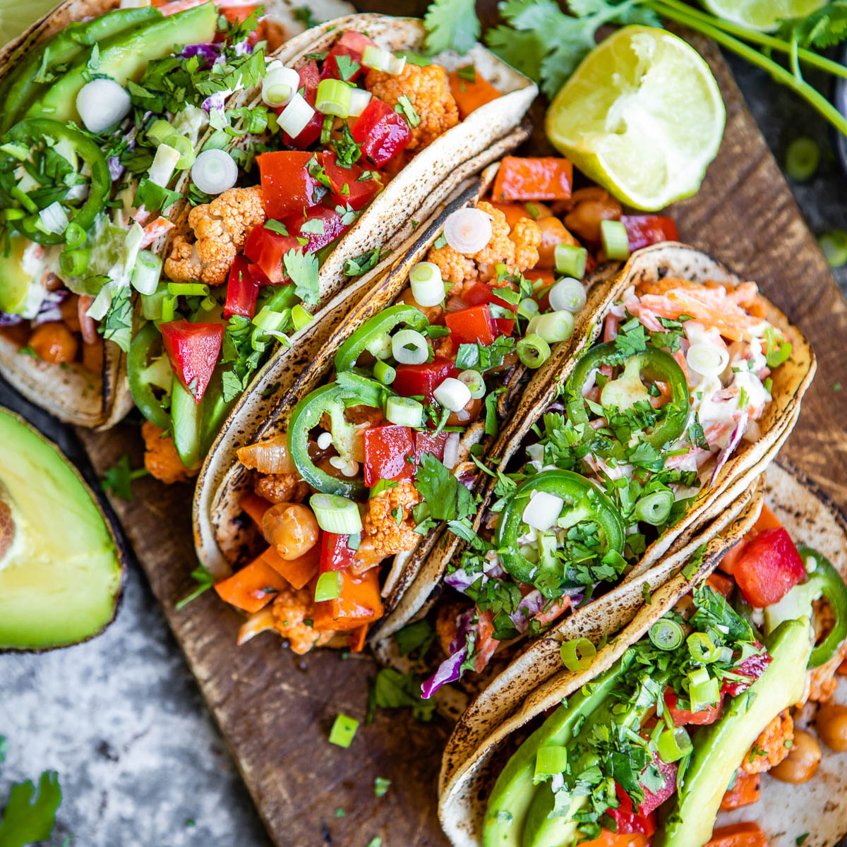 several vegetarian tacos in a row on a wooden board.