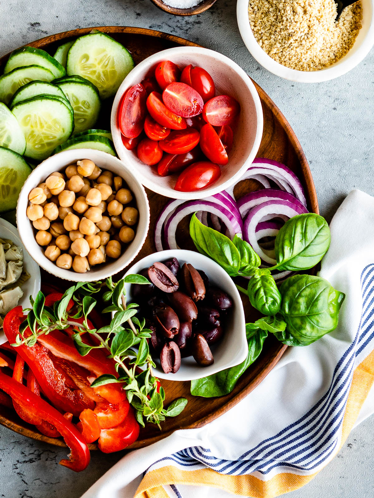 small white bowls of tomatoes, chickpeas and olives along with other gatherings of purple onion, cucumber, basil and peppers, ingredients commonly found in vegetarian Mediterranean recipes.