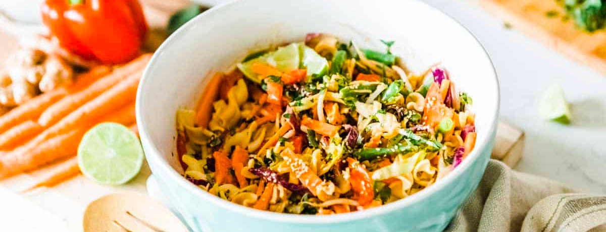 bowl of vegetarian noodle salad with fresh vegetables out of focus in the background