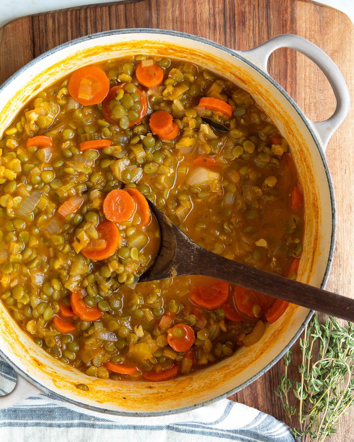 Cooked vegetable split pea soup getting stirred by a wooden spoon in a white stock pot.