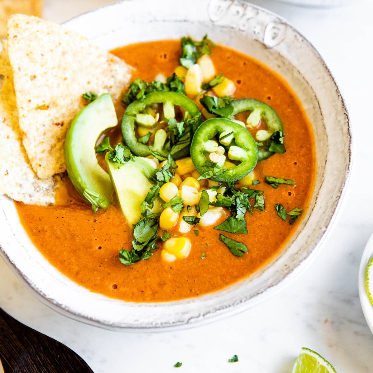 Bowl of vegetarian tortilla soup topped with peppers and tortilla chips.