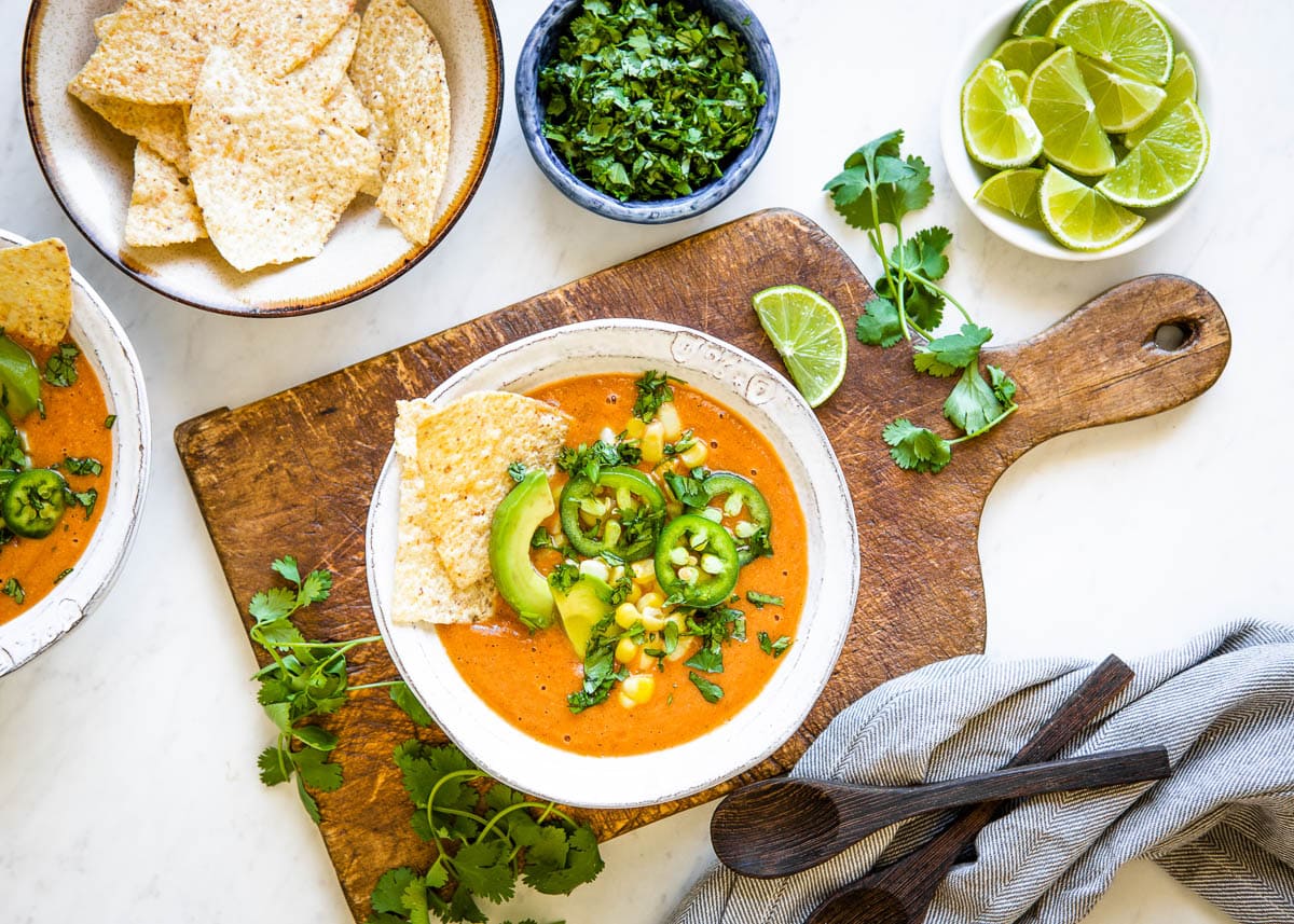 delicious vegan soup in a white bowl with tortilla chips, fresh jalapeños, avocados, corn and cilantro on top.