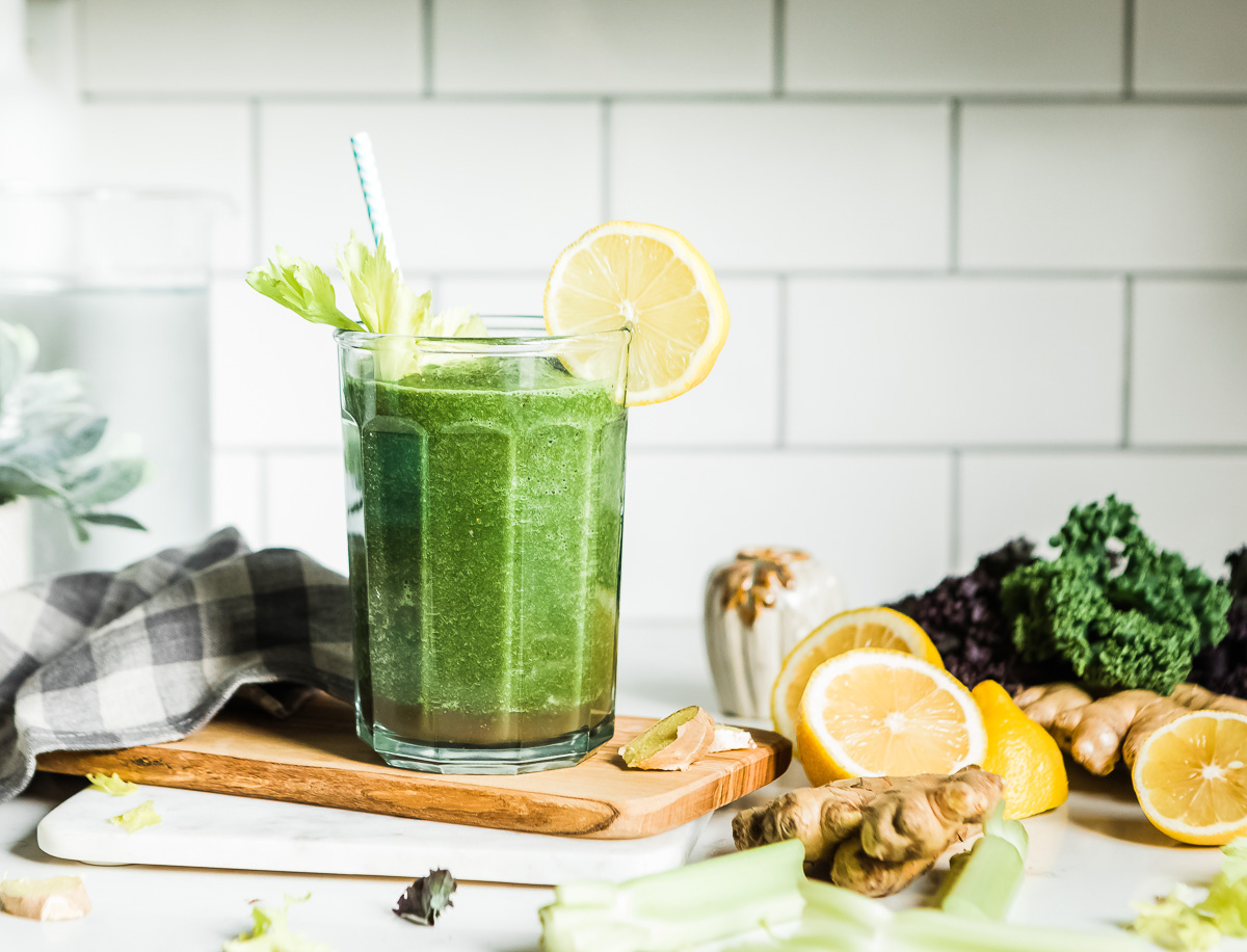 Green veggie fruit smoothie in a glass with a straw