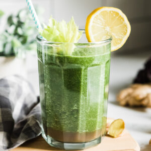 Veggie fruit smoothie in a glass garnished with celery leaf and a lemon round