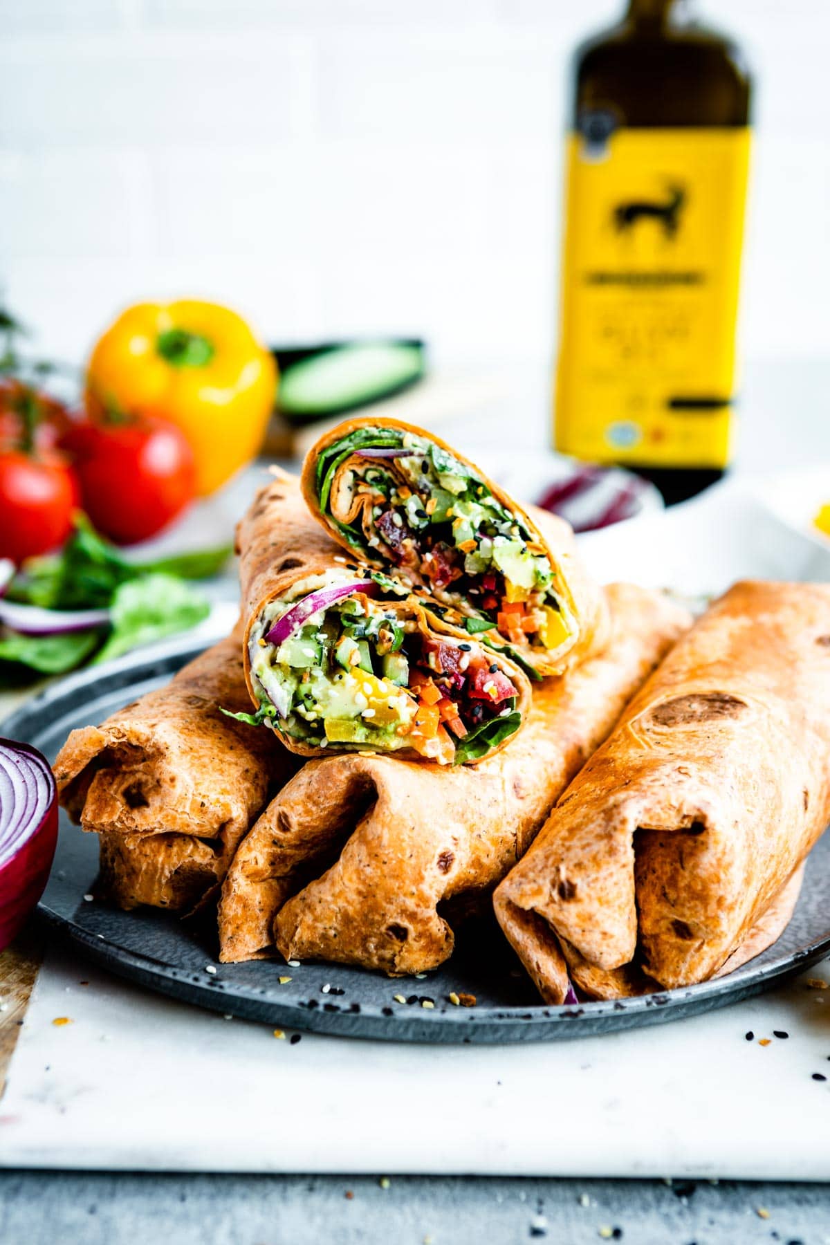 Sliced best veggie wrap, on top of 3 full wraps on a gray plate, veggie wrap ingredients are blurred in the background.