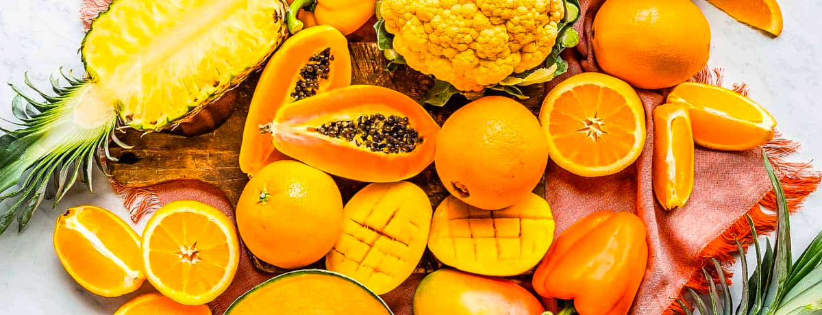 variety of orange/yellow ingredients on a table: papaya, oranges, mango, pineapple, yellow cauliflower, orange pepper, and more