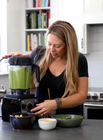 white woman using a vitamix blender to make a green smoothie in a kitchen.