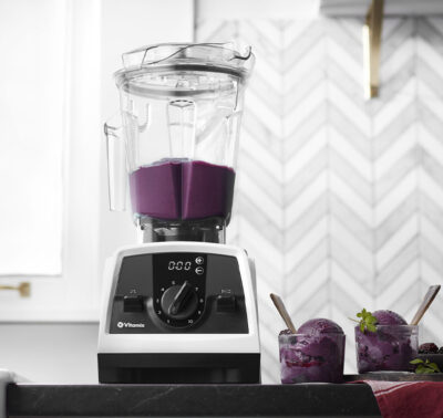 White blender with purple smoothie content on a black countertop with sorbet in a glass