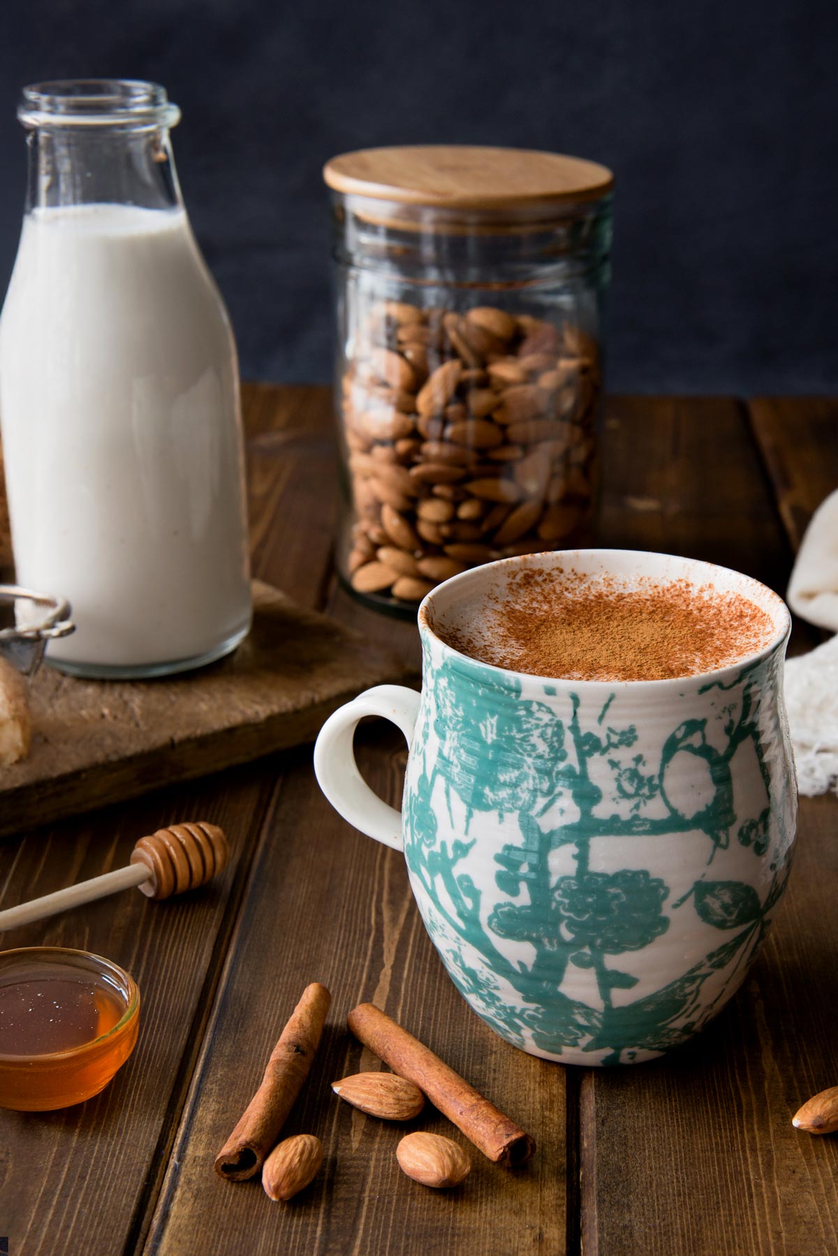 A selection of ingredients for a soothing bedtime drink, including a bottle of almond milk, small bowls of ground ginger, ground cinnamon, and a pinch of cayenne pepper.\\