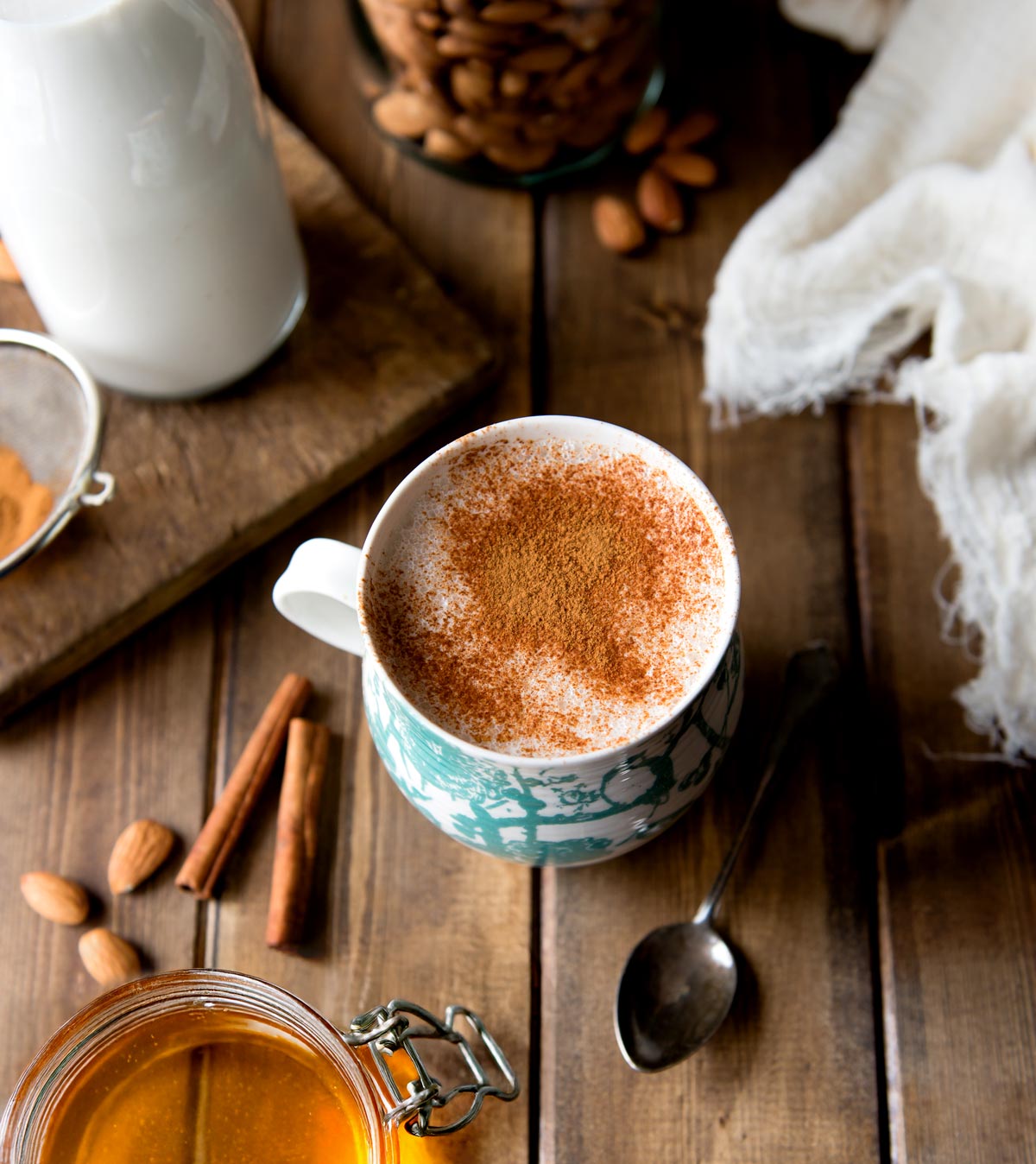 Rustic wood table with mug of warm almond milk and jar of honey.