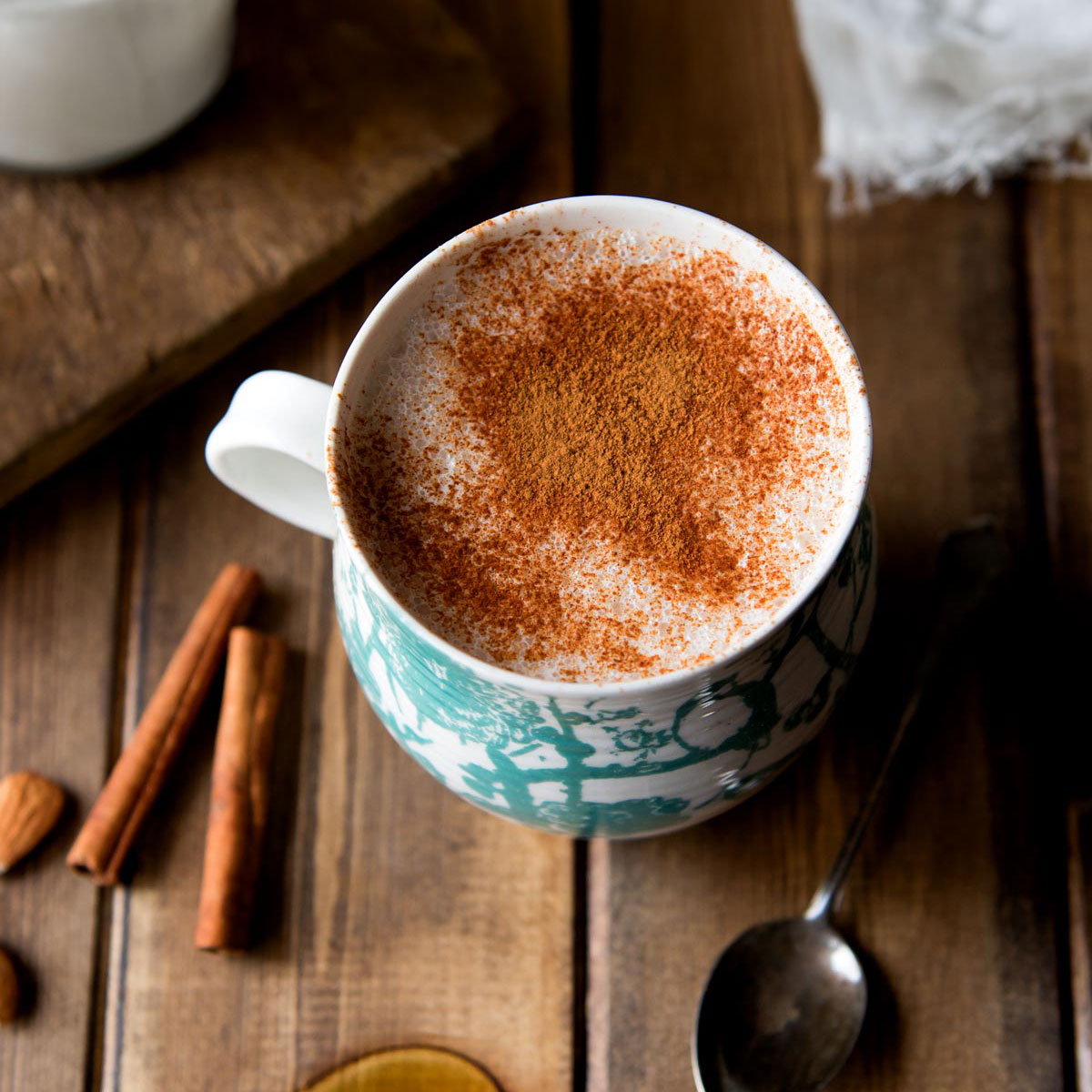 A cozy cup of warm almond milk topped with a sprinkle of cinnamon, served in a rustic white mug.