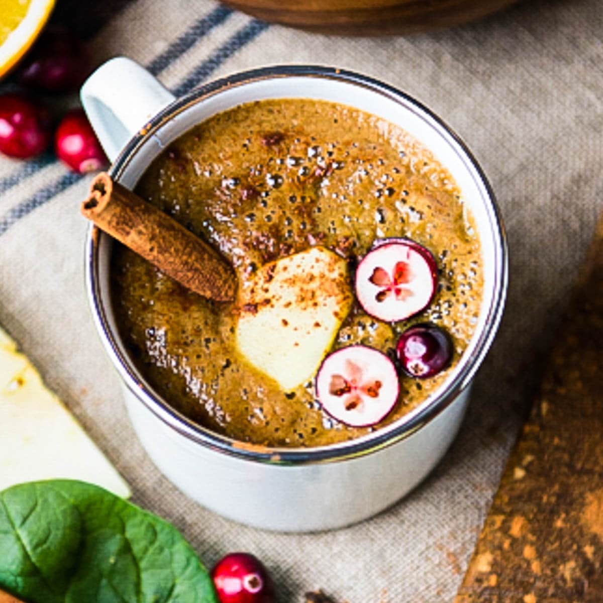 warm smoothie in a mug topped with fresh cranberries and a cinnamon stick.
