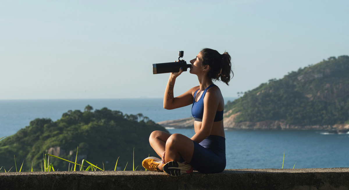 Woman in workout clothes outside drinking from a water bottle.