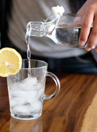 Pouring water into. glass with ice and lemon while using water intake calculator.