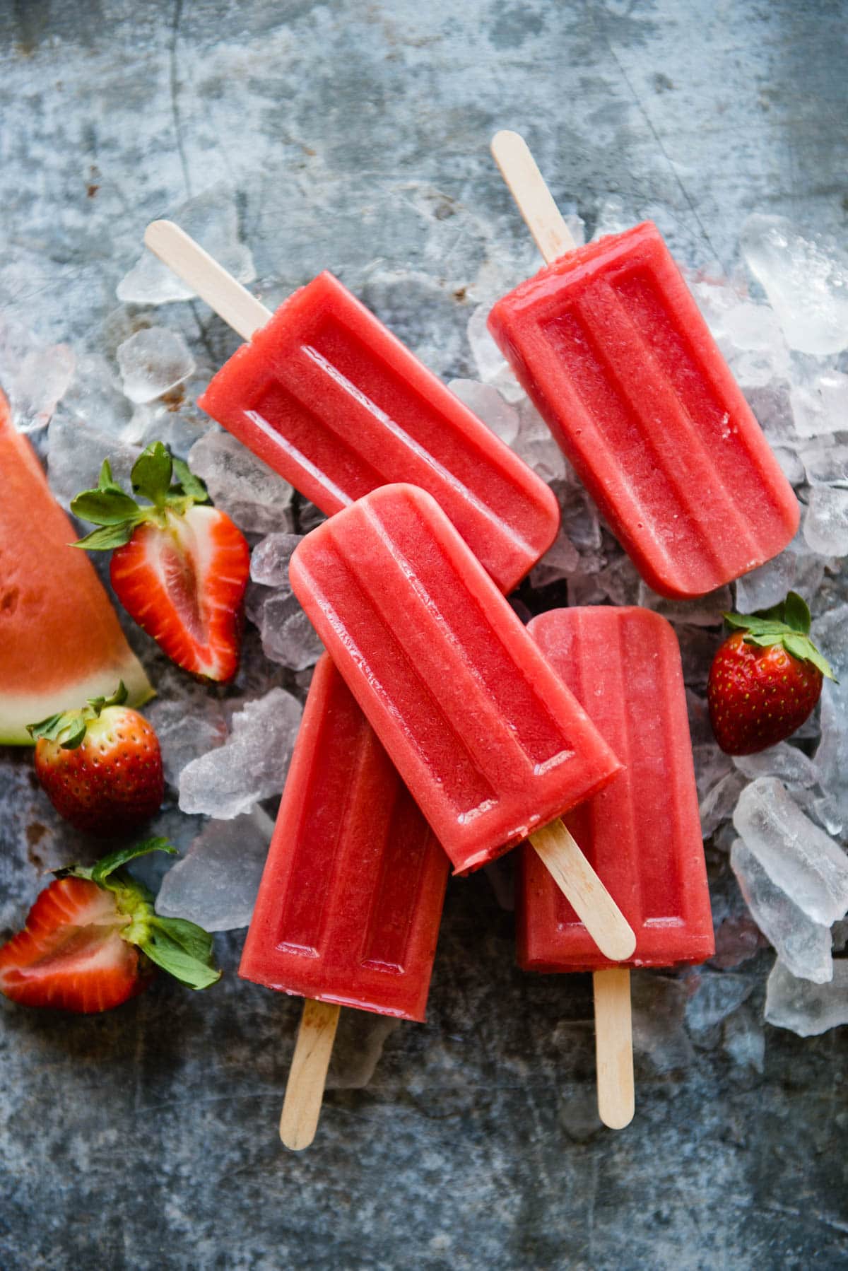 red fruit popsicles sitting on ice surrounded by strawberries and watermelon.