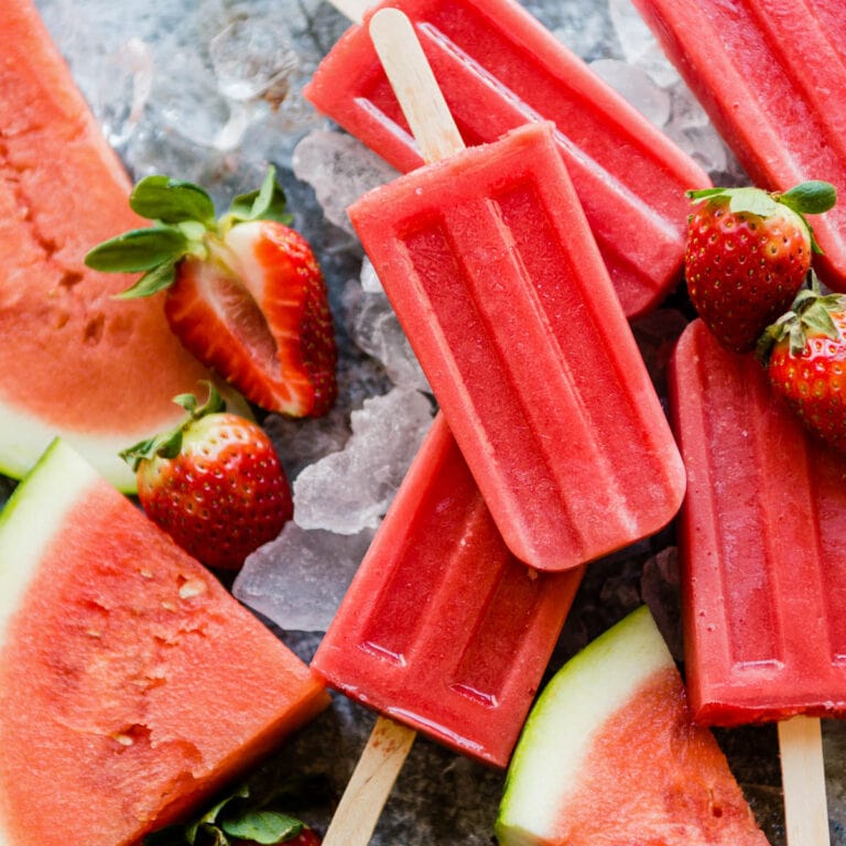 fresh watermelon popsicles sitting on ice with fresh strawberries and watermelon slices.