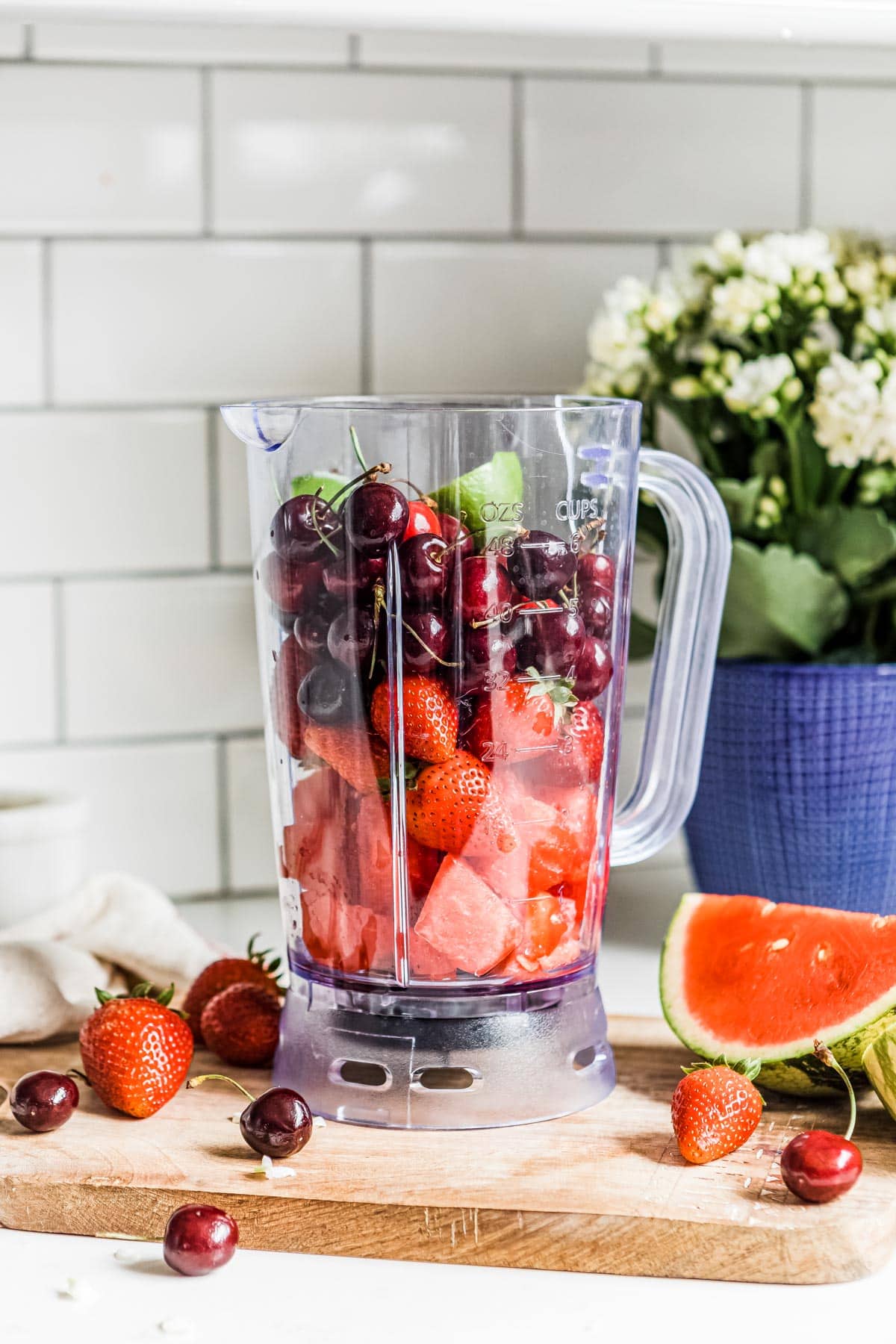 whole ingredients in a blender container including lime, cherries, strawberries and watermelon.