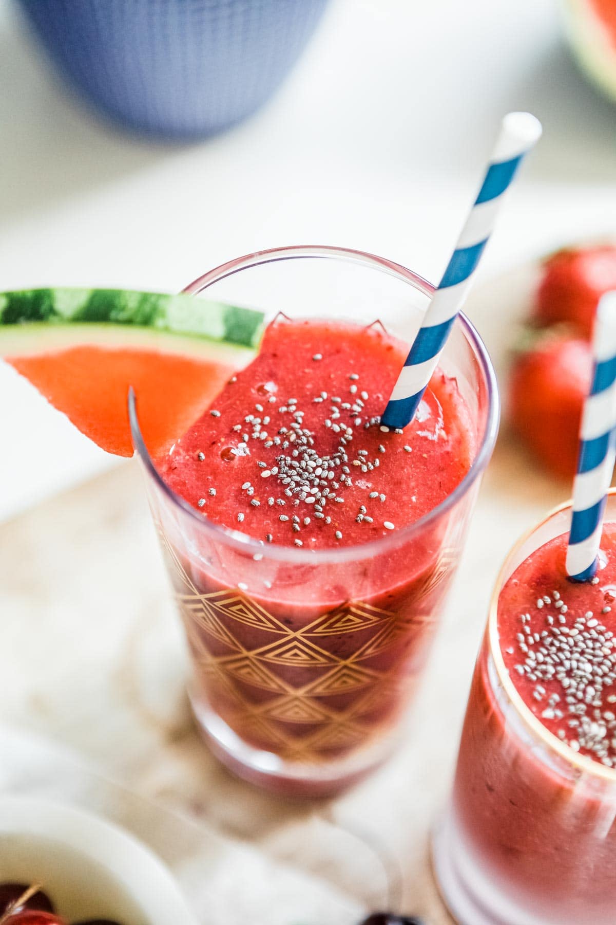 watermelon smoothie with chia seeds sprinkled on top in a glass with a paper straw.