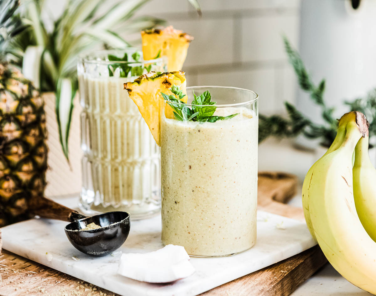 weight gain smoothie in glass with fresh pineapple and mint on top, next to a scoop of protein powder.