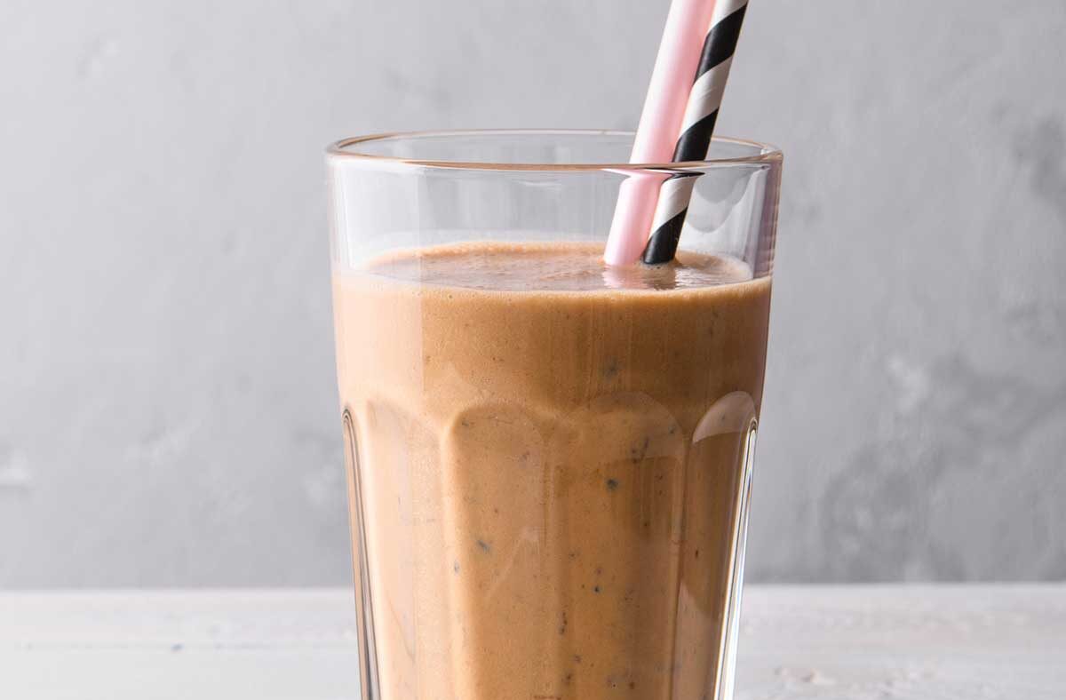 Glass of a delicious chocolate weight loss shake with a pink straw and a black and white striped straw