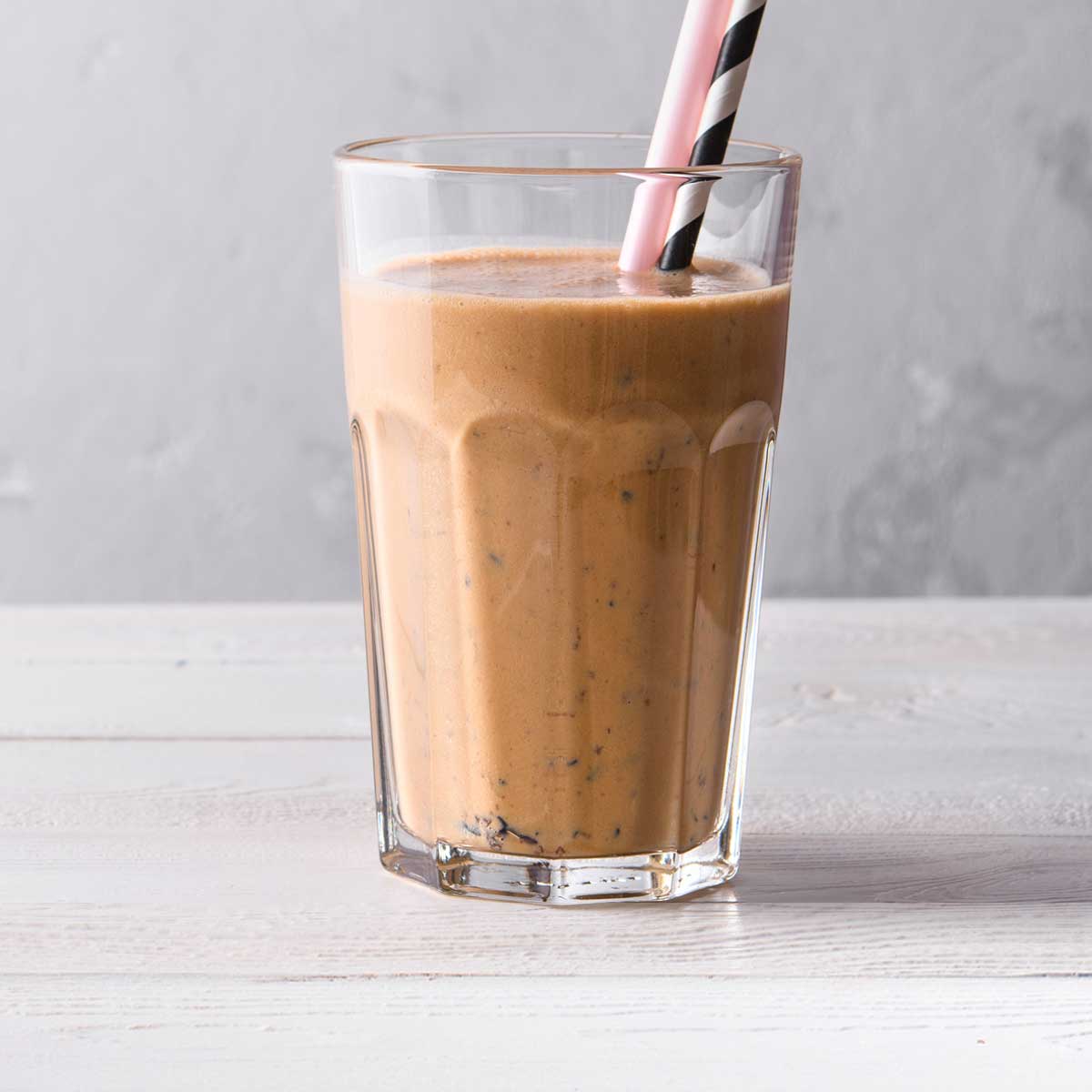 chocolate smoothie in a glass cup with a pink smoothie straw.